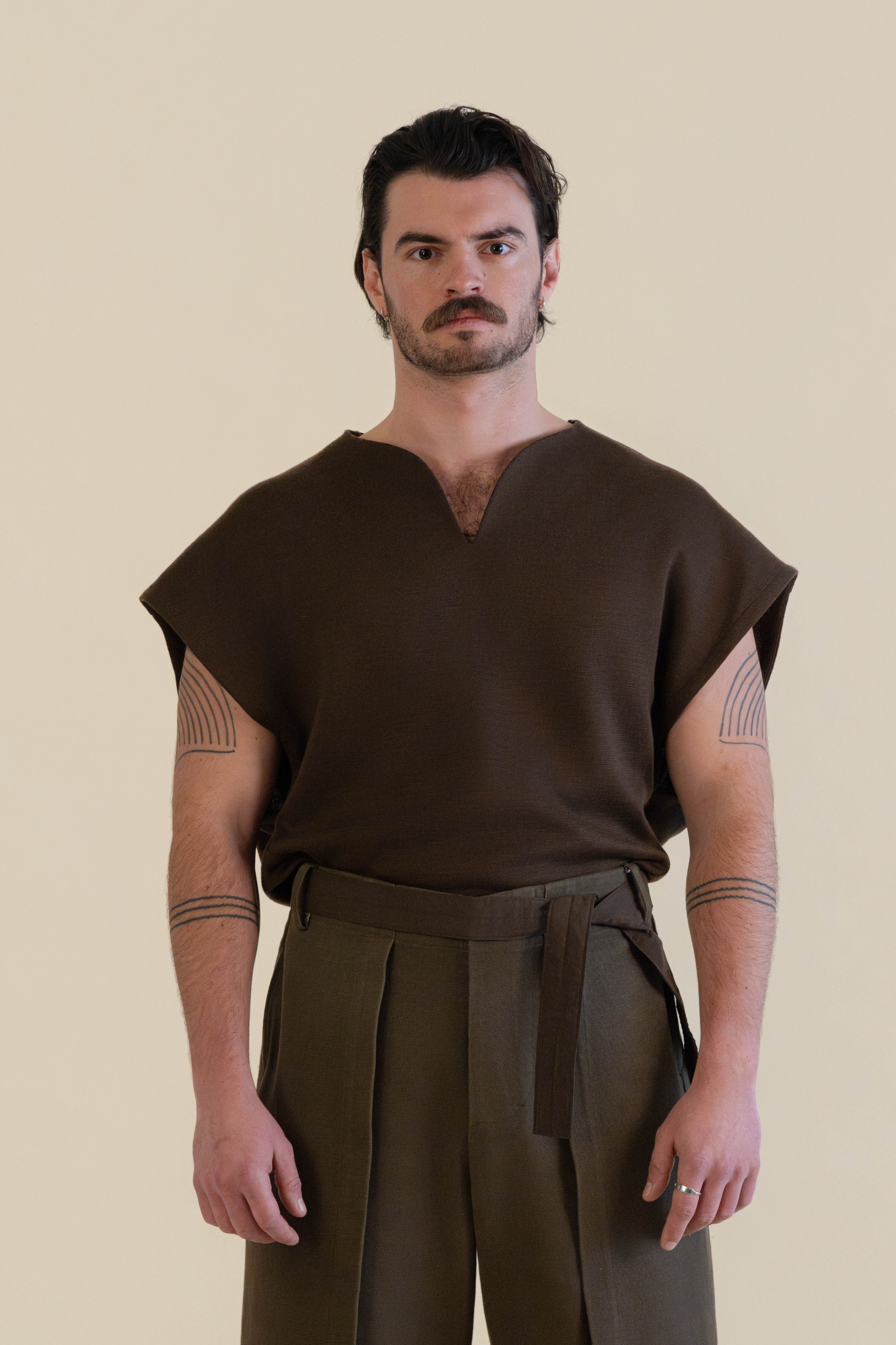 Male model wearing brown knit top and trousers in soft warm light, Oniri editorial aesthetic