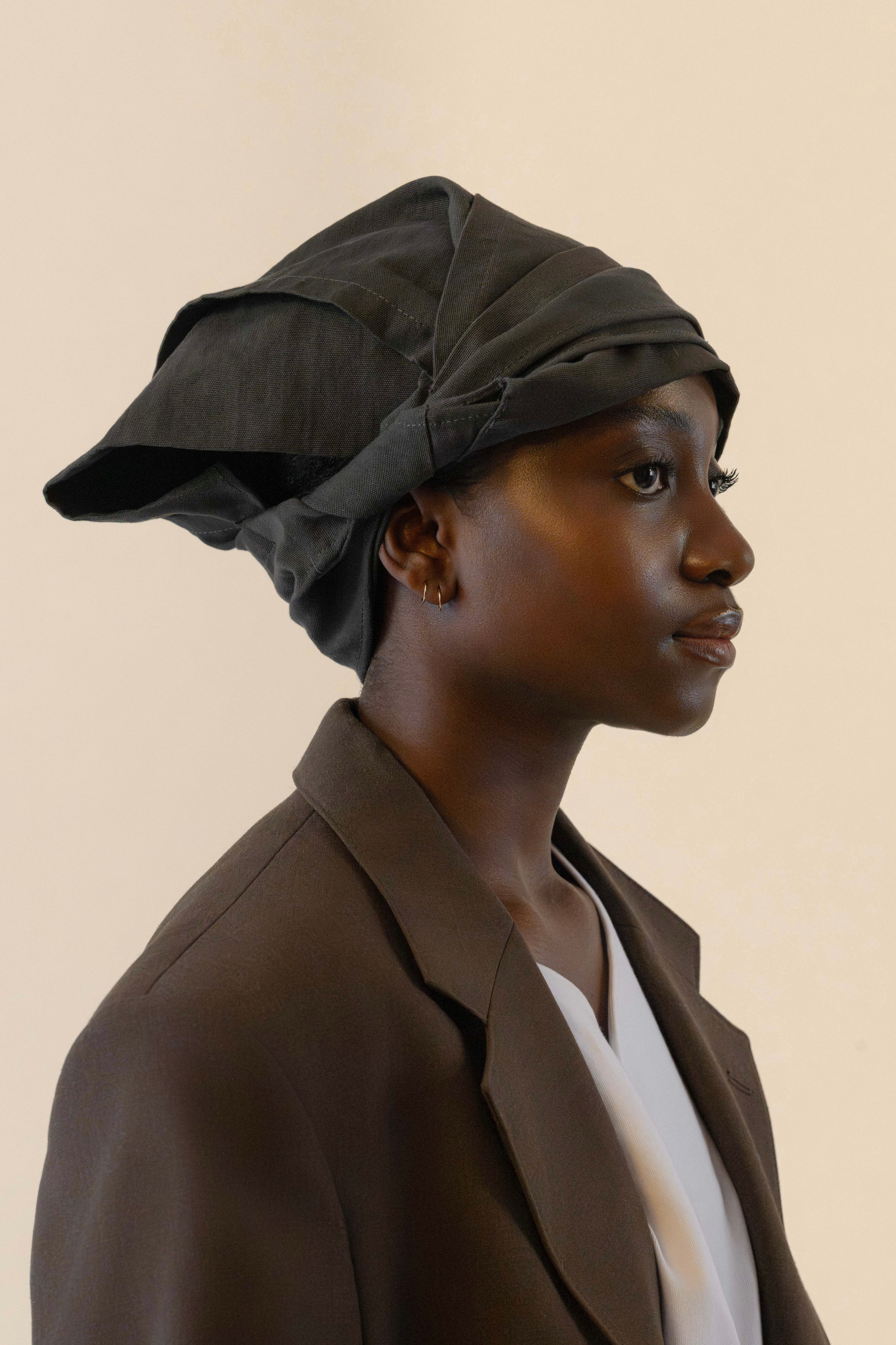 Side profile of female model wearing grey twisted bandana and brown blazer in soft warm light, Oniri editorial aesthetic