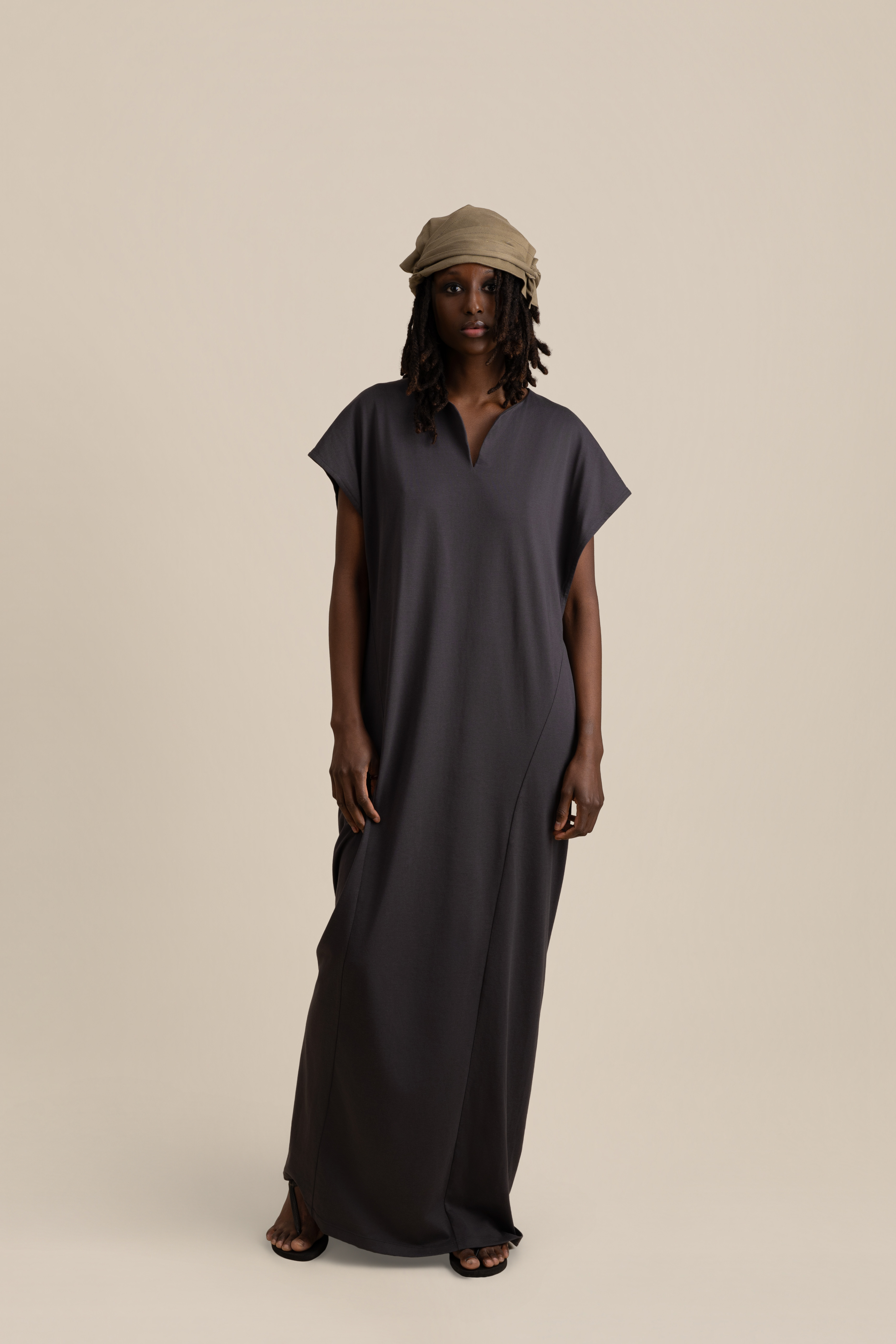 Front view of male model wearing grey Light U-neck Tunic, taupe twisted bandana and brown trousers in soft warm light, Oniri editorial aesthetic