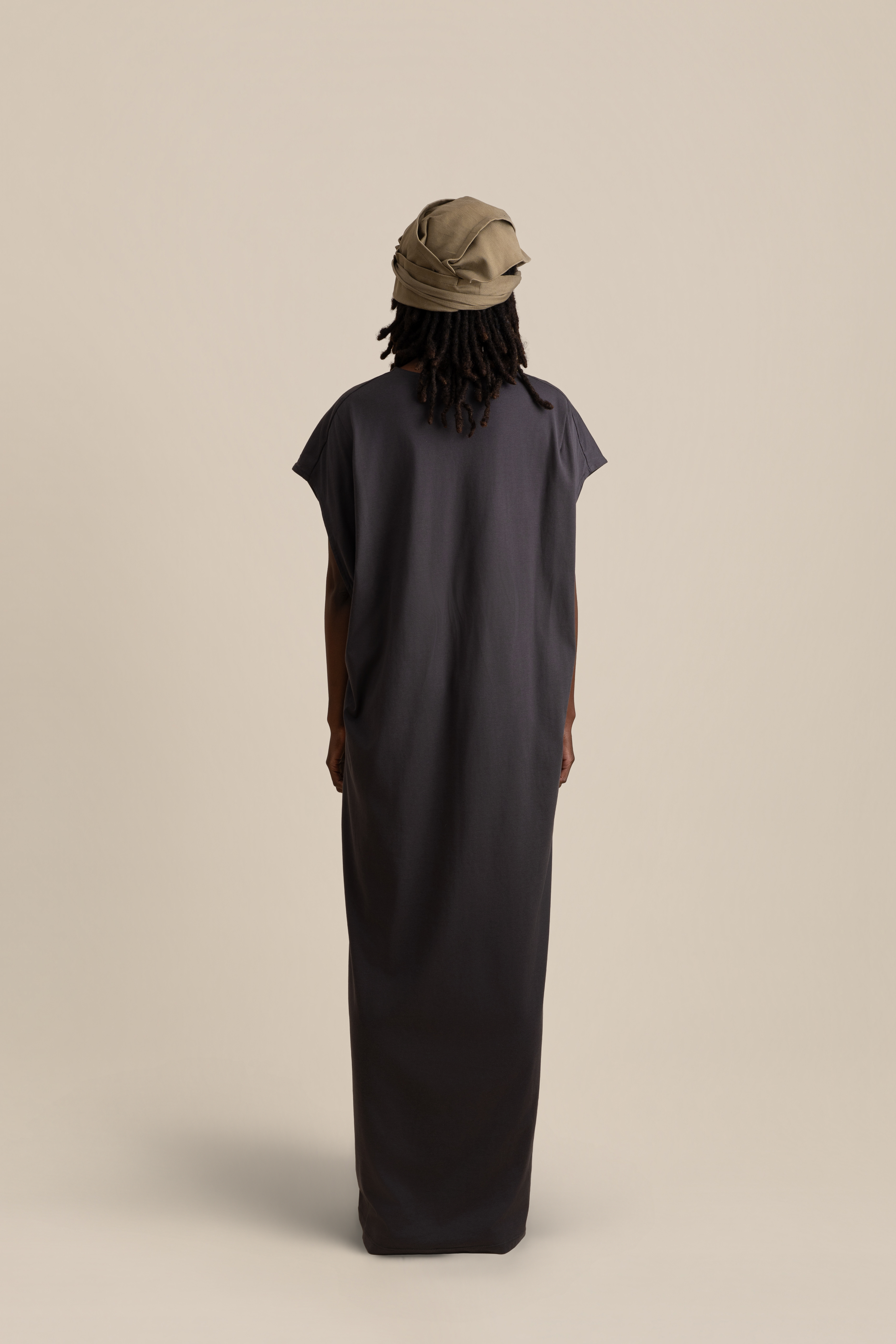 Front half-body view of male model wearing grey Light U-neck Tunic, taupe twisted bandana and brown trousers in soft warm light, Oniri editorial aesthetic