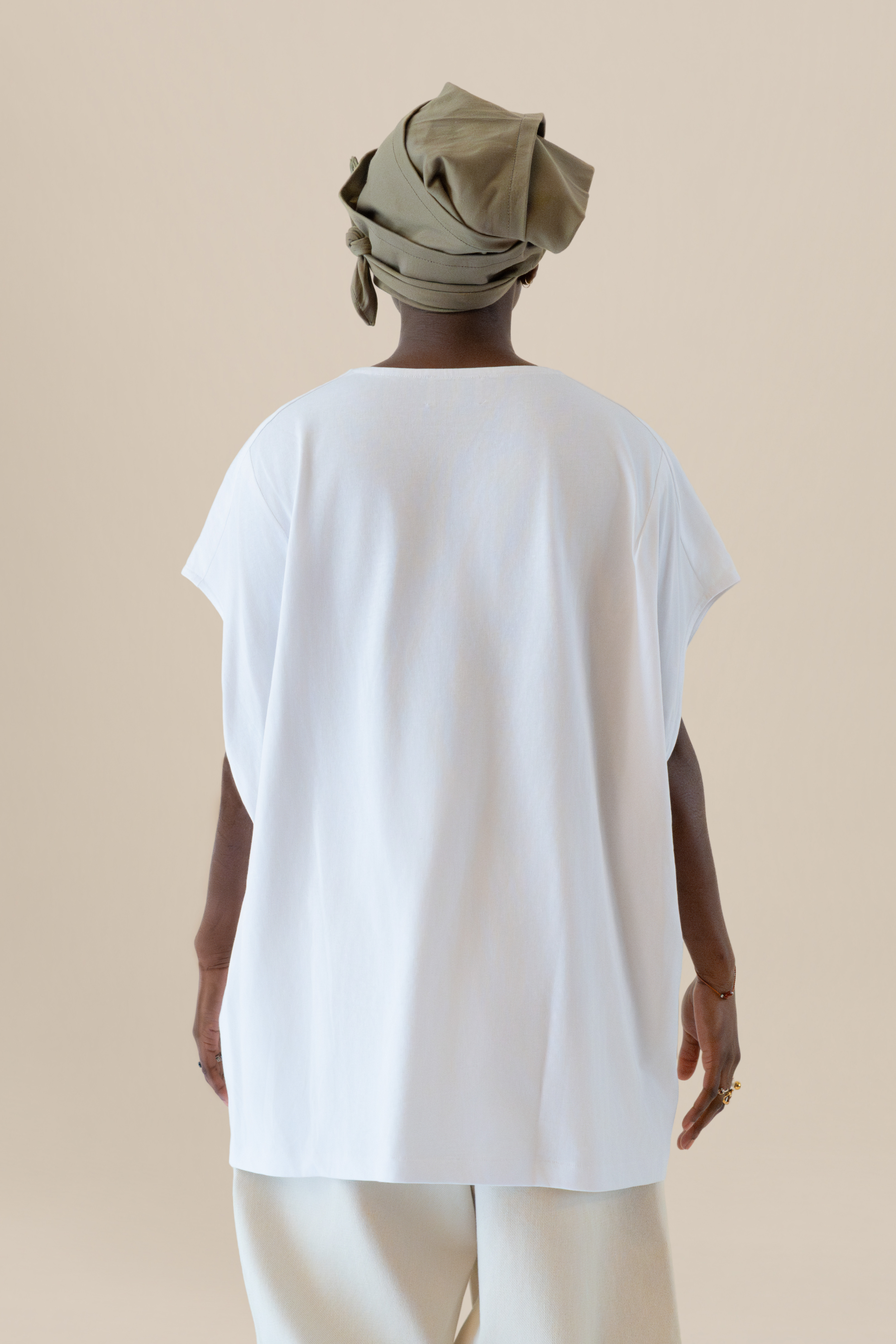 Back view of female model wearing the Light U-neck Tunic in white with grey twisted bandana, soft warm light, Oniri editorial aesthetic