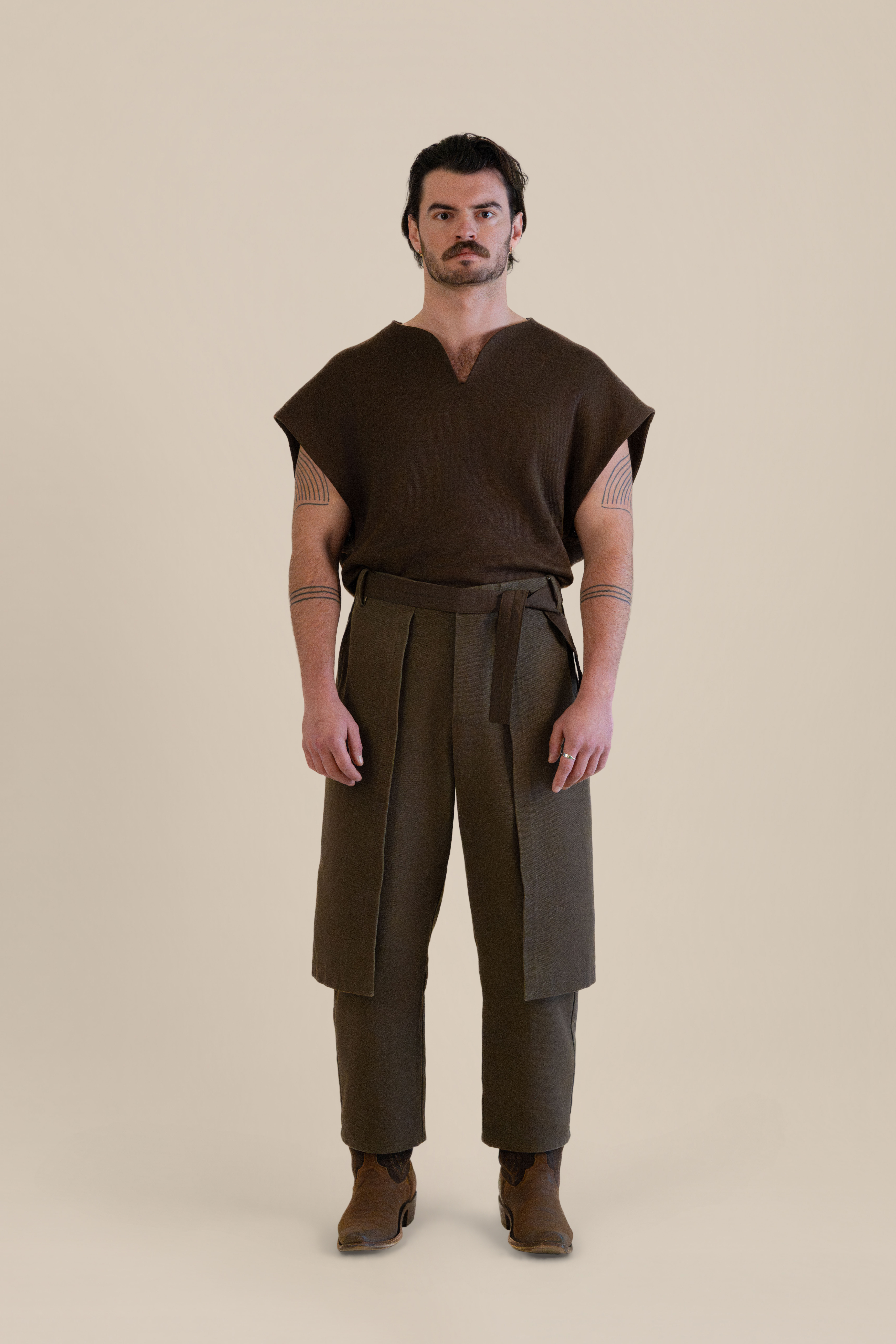 Full-body front view of male model wearing brown Cowboy Pants and brown knit top in soft warm light, Oniri editorial aesthetic