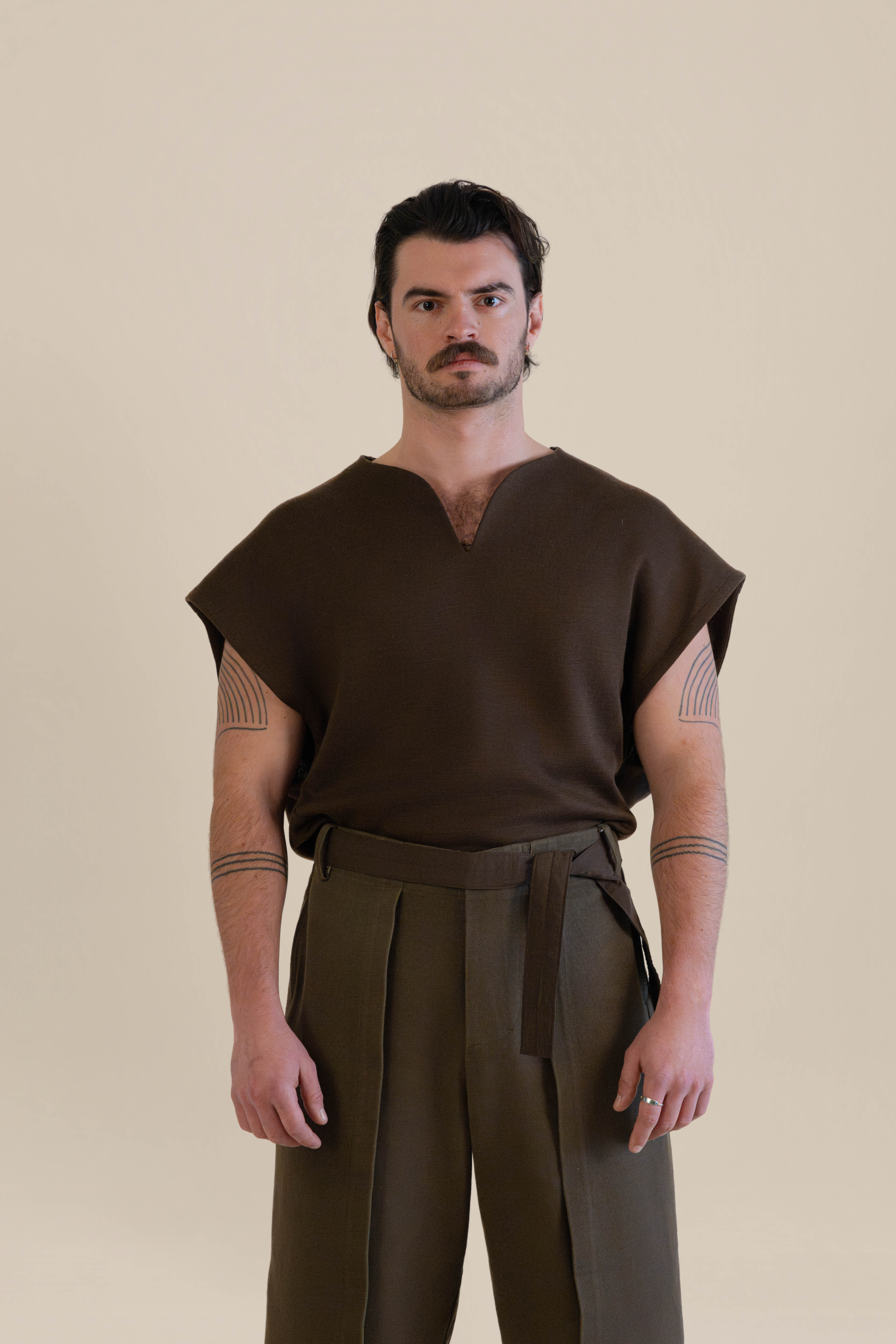 Male model wearing brown knit top and trousers in soft warm light, Oniri editorial aesthetic