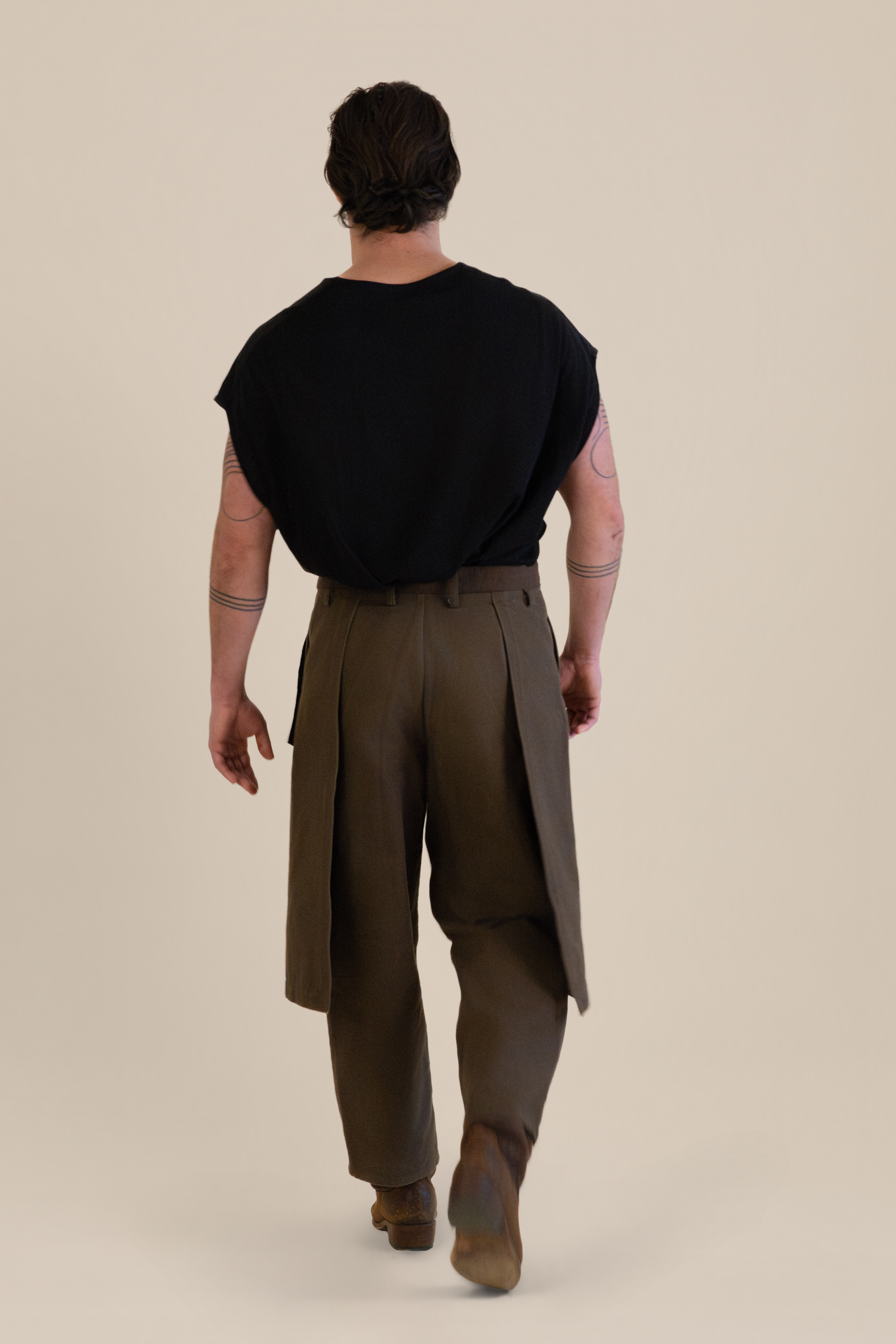 Back view of male model walking away wearing brown Cowboy Pants and black top in soft warm light, Oniri editorial aesthetic