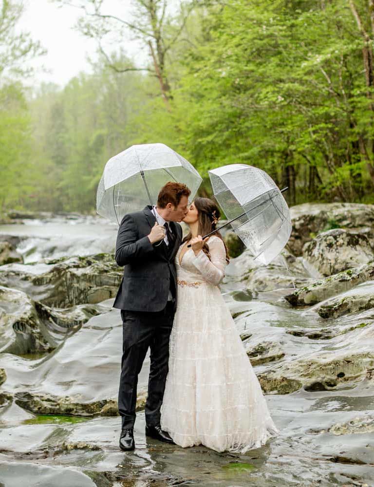 A couple posing in a river holding umbrellas