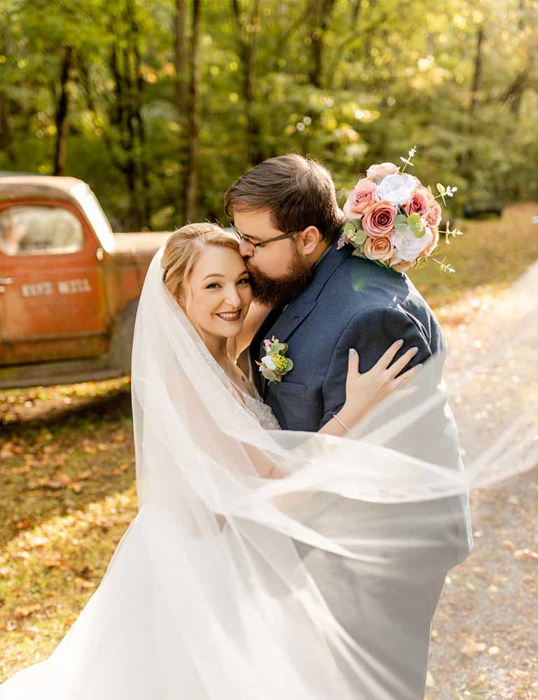 An eloped couple posing in front of an old truck at Elly's Mill