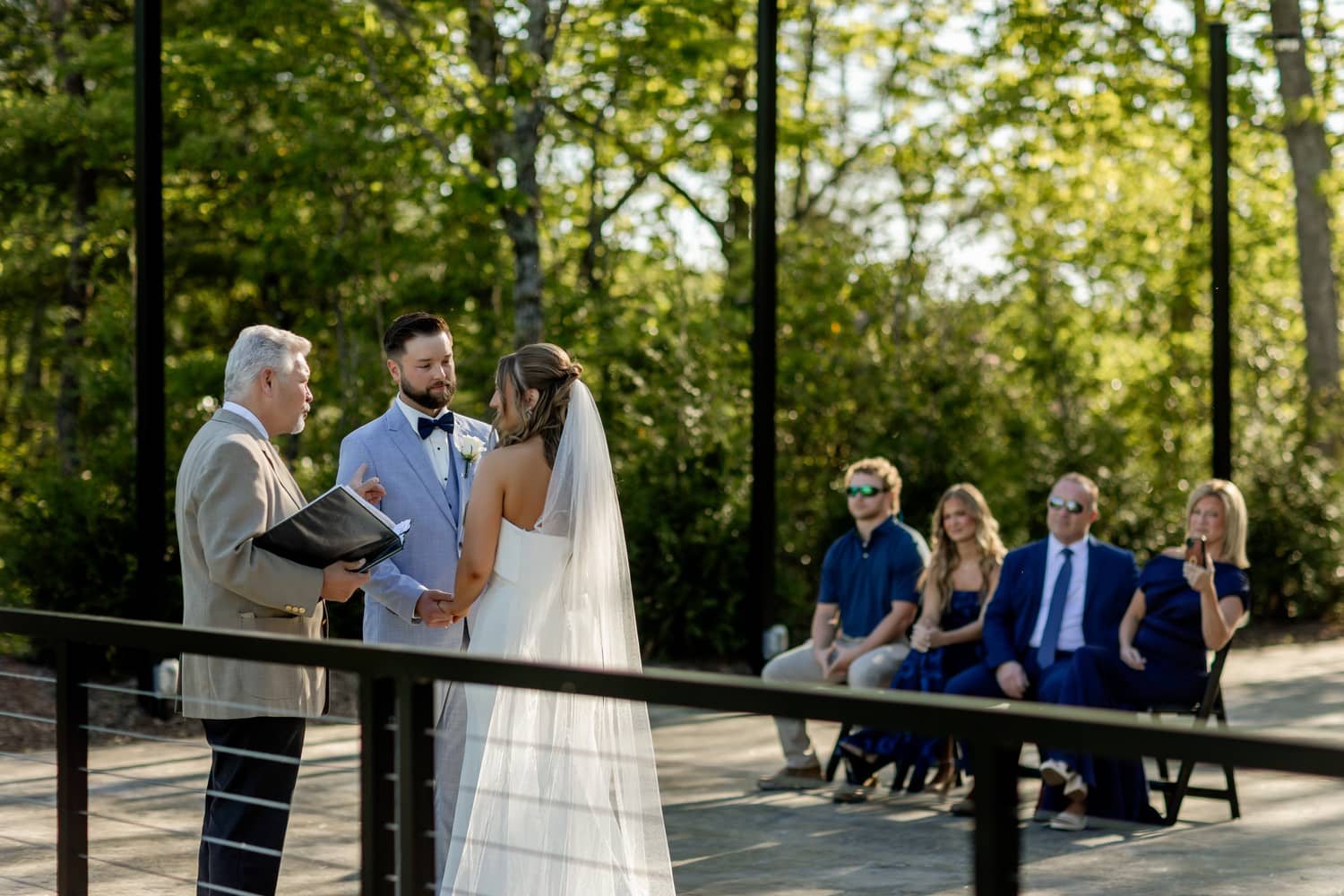 A couple exchanges vows during an outdoor elopement ceremony, surrounded by guests in a lush, green setting at Trailhead Venues..