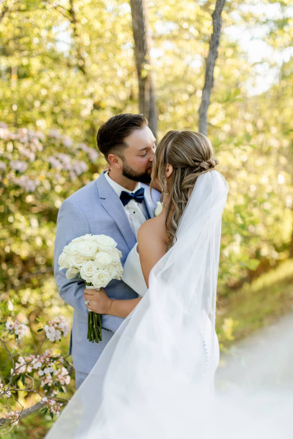A couple shares a kiss in a sunlit forest, surrounded by trees, celebrating their elopement.