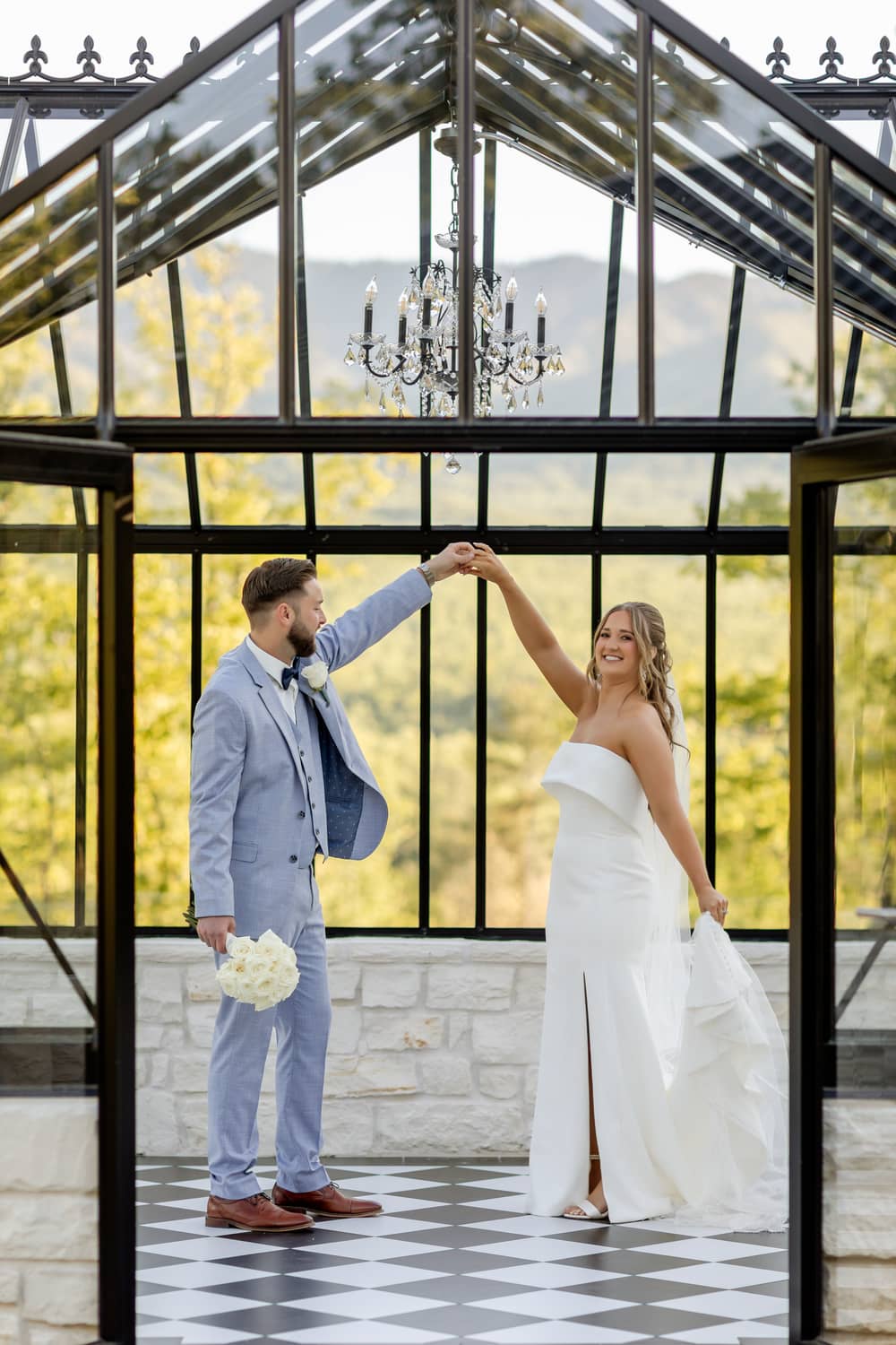 A couple in formal attire dances inside a glass venue, surrounded by vibrant foliage in the Smoky Mountains.