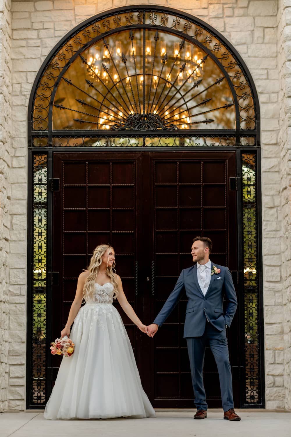 A couple holding hands in front of an ornate entrance, dressed for their elopement in the Smoky Mountains.