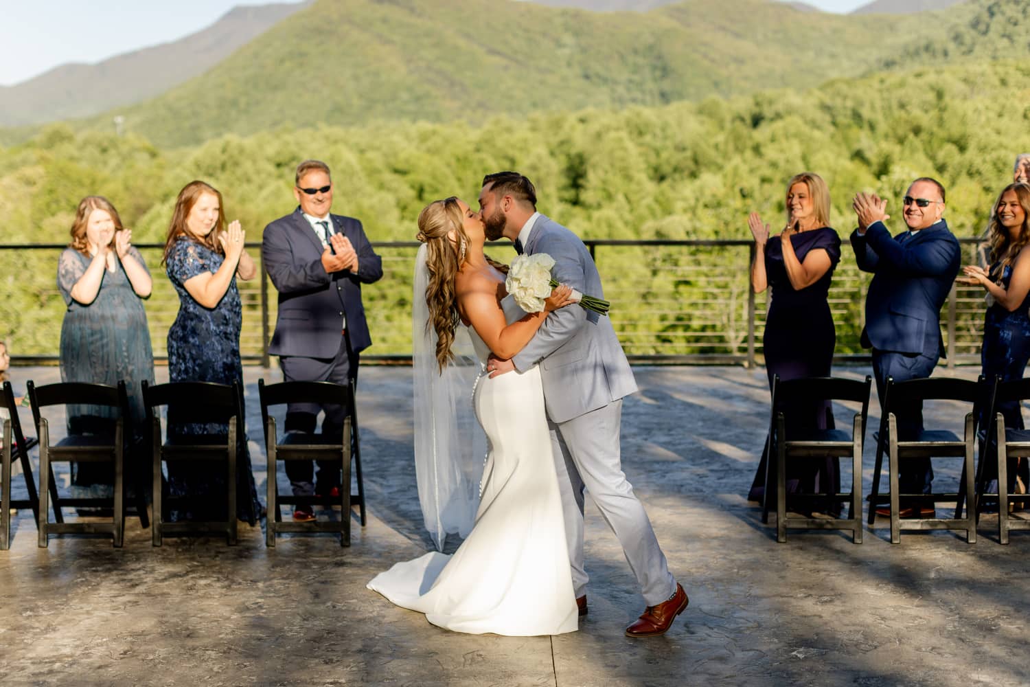 A couple shares a kiss during their elopement ceremony, surrounded by guests in a scenic setting with mountain views at Trailhead Venues.