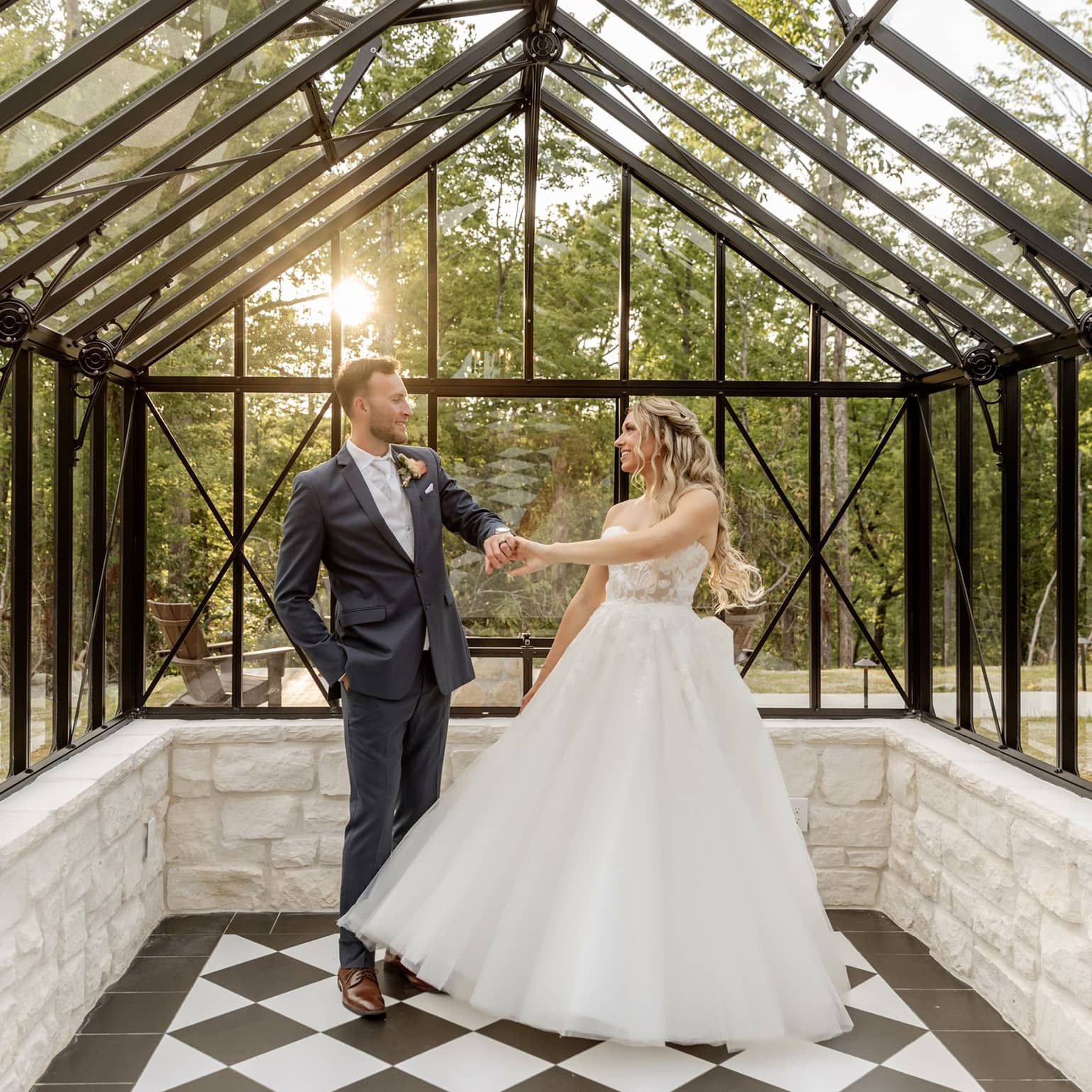 A couple in formal attire dances inside a glass venue greenhouse, surrounded by vibrant foliage in the Smoky Mountains.