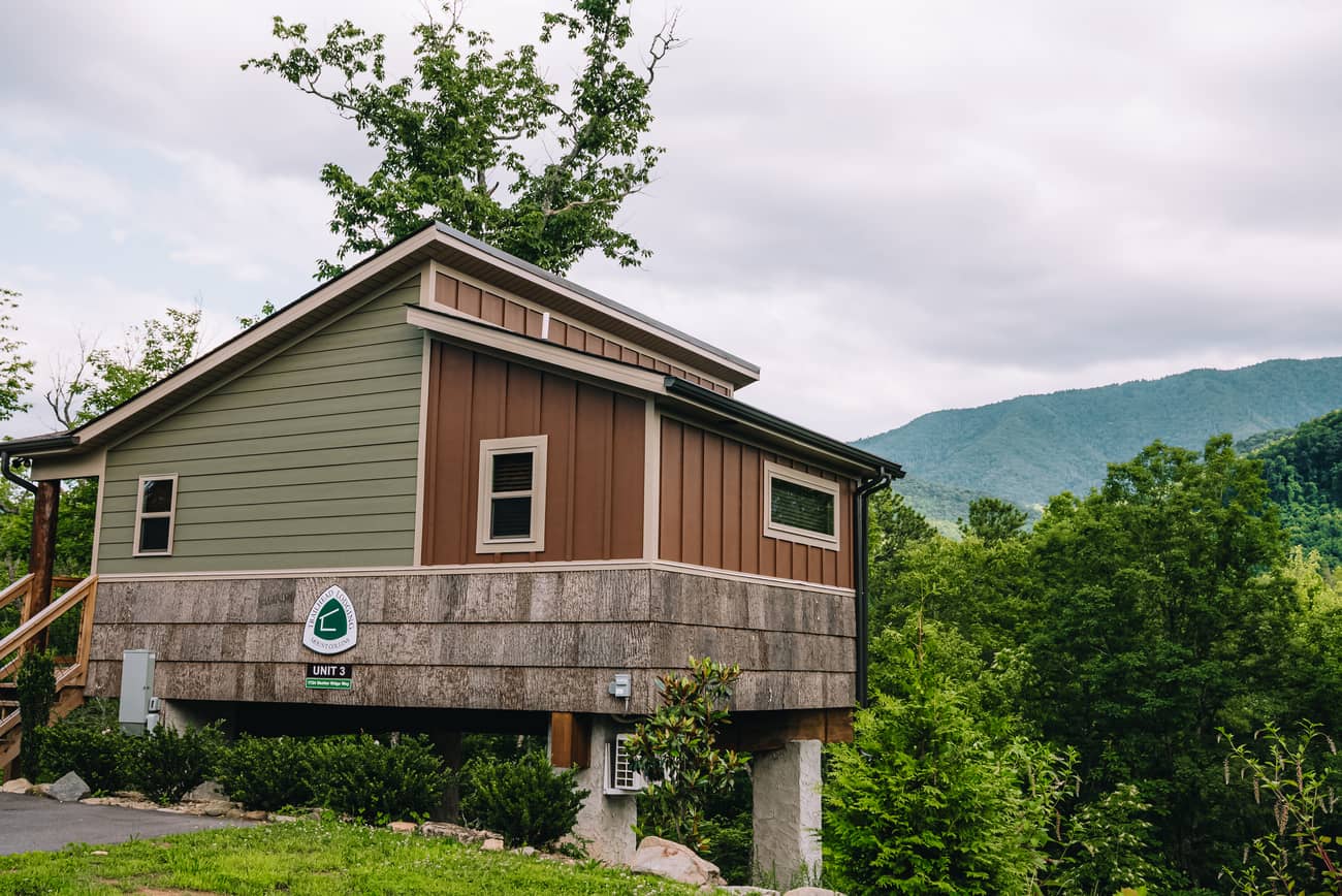 Cozy, elevated, small cabin with greenery and mountains in the background