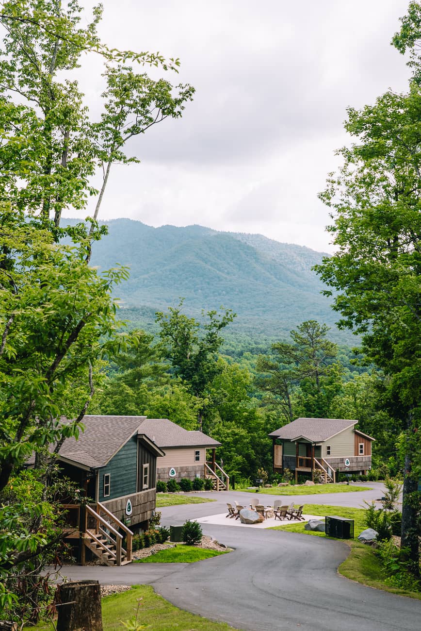 Road leading to rental cabins and a fire pit surrounded by trees with Smoky Mountains backdrop.