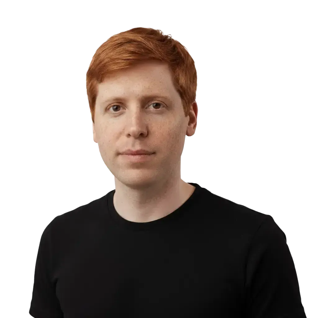 Portrait of a young man with red hair and fair skin wearing a black shirt, looking at the camera.