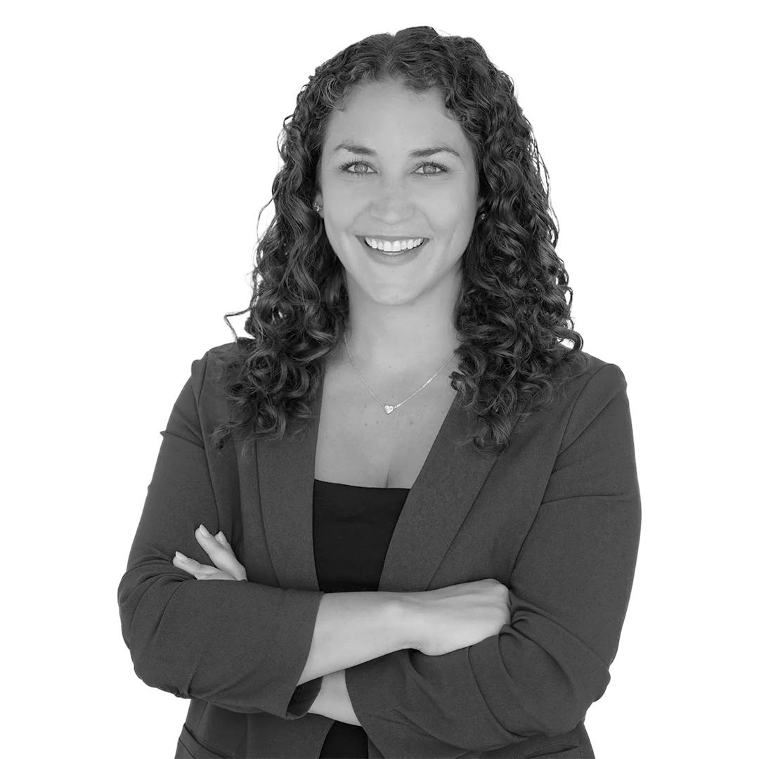 Smiling woman with curly hair wearing a blazer and crossed arms.