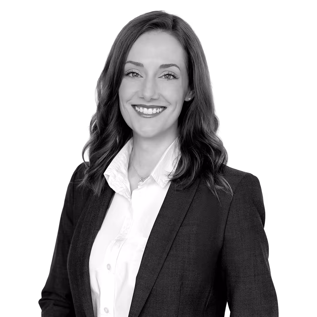 Smiling woman with wavy hair wearing a dark blazer and white collared shirt against a white background.