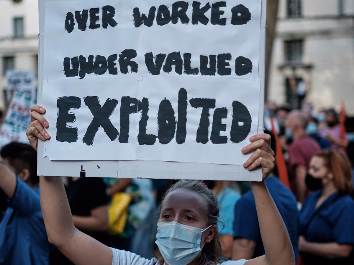 A protester holding a sign reading "Overworked, undervalued, exploited."
