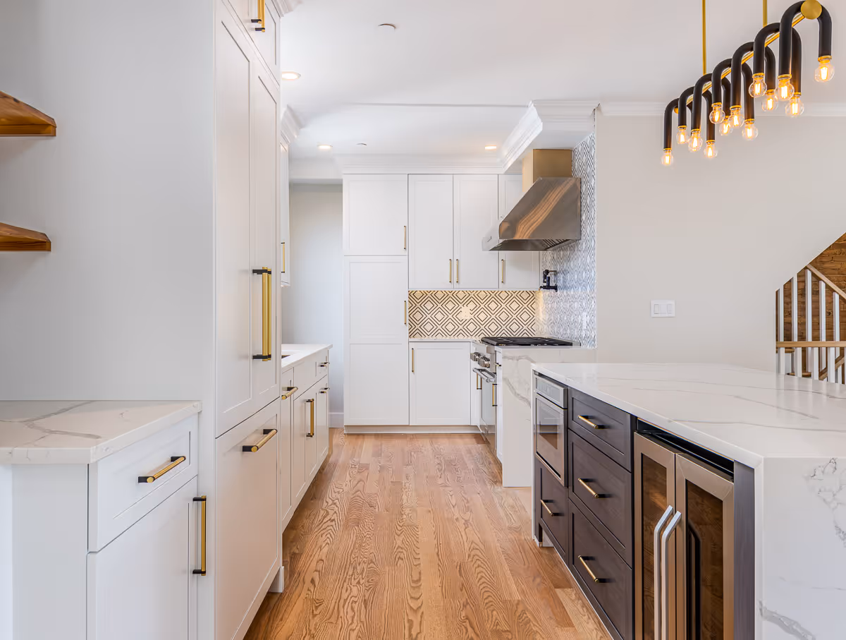 Bright modern kitchen with white cabinets, wood flooring, and pendant lights – real estate photo