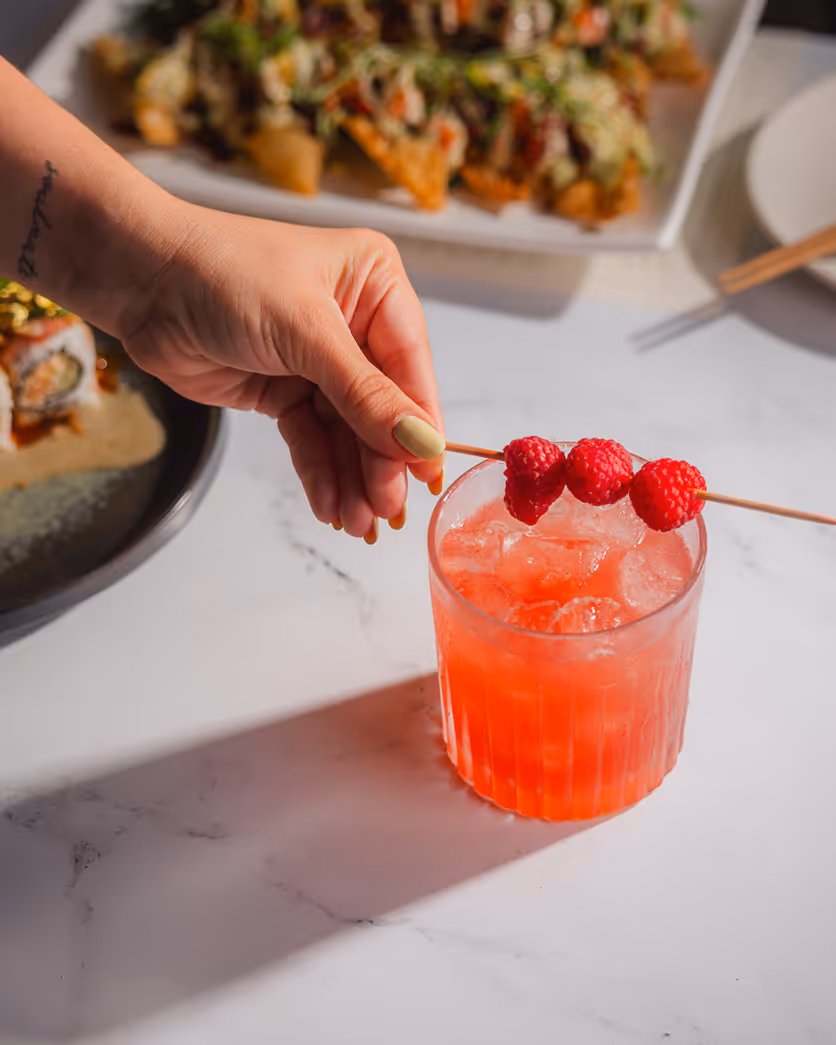 Boston food photography featuring a hand holding a red cocktail with skewered berries at a restaurant table.