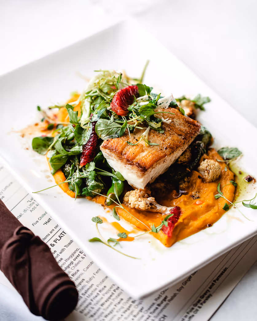 Boston restaurant photographer capturing plated fish dish with greens and orange puree in natural light.