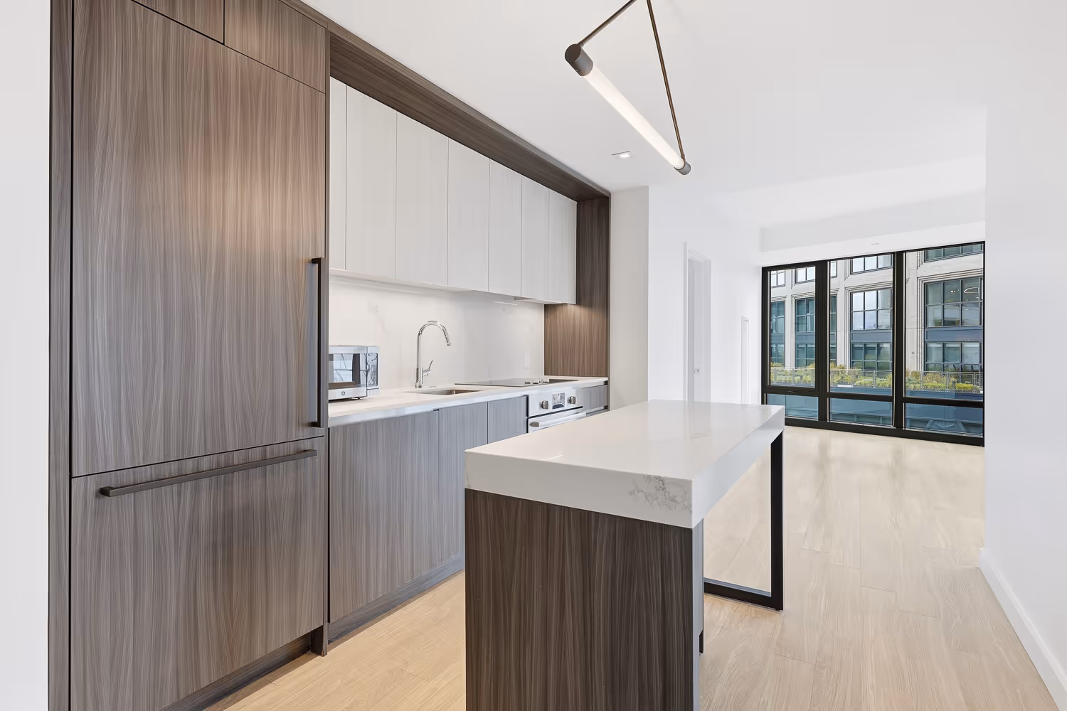 Modern kitchen with wood-paneled cabinets, white marble countertops, built-in oven, and large windows overlooking an urban building.