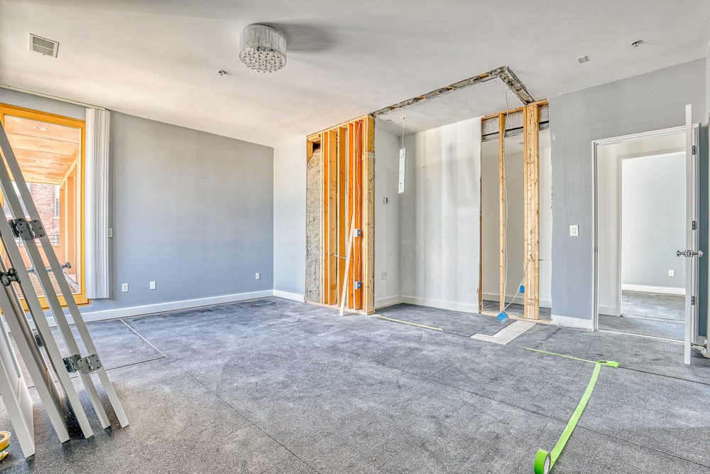 Bedroom during renovation with partial framing exposed and construction materials on site.