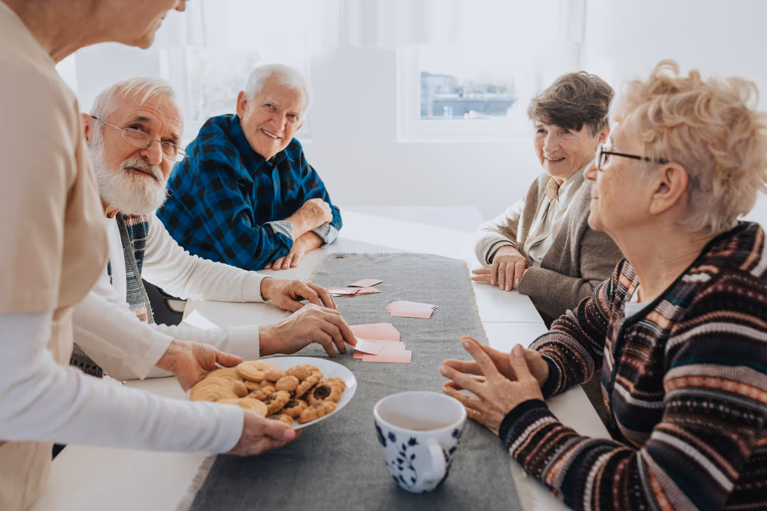 A group of elderly people enjoying cookies together at a table, sharing smiles and conversation.
