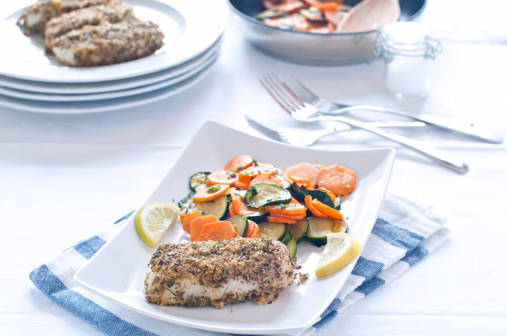 A serving of fish with assorted vegetables on a plate, with a fork placed next to the dish.
