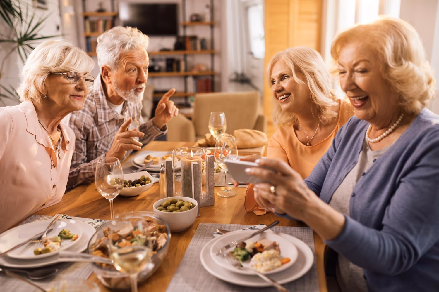 A group of senior individuals enjoying dinner together at a warmly lit table, sharing laughter and conversation.