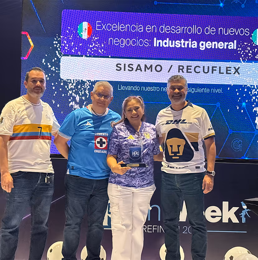 Cuatro personas posan sonrientes en un escenario frente a una pantalla que reconoce la excelencia en desarrollo de nuevos negocios en industria general, sosteniendo un trofeo.