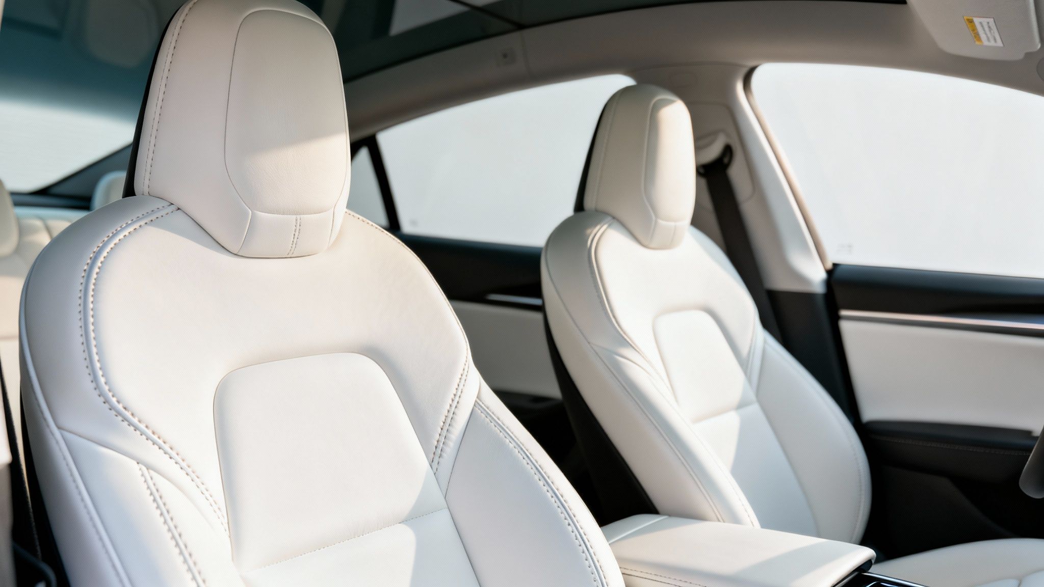 Close-up of clean white leather interior car seats with visible stitching.