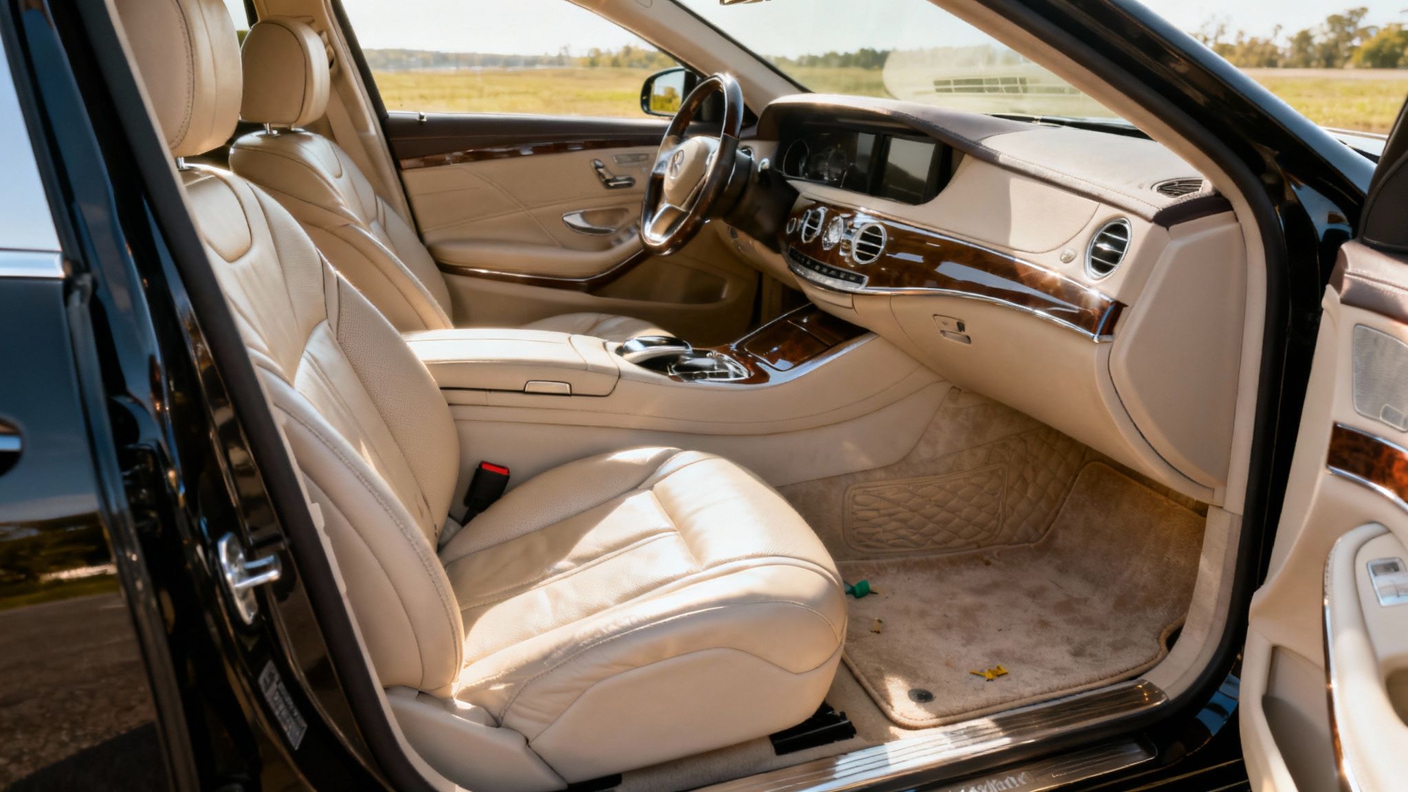 Luxurious beige leather interior of a Mercedes-Benz car with wooden trim, seen through an open door.