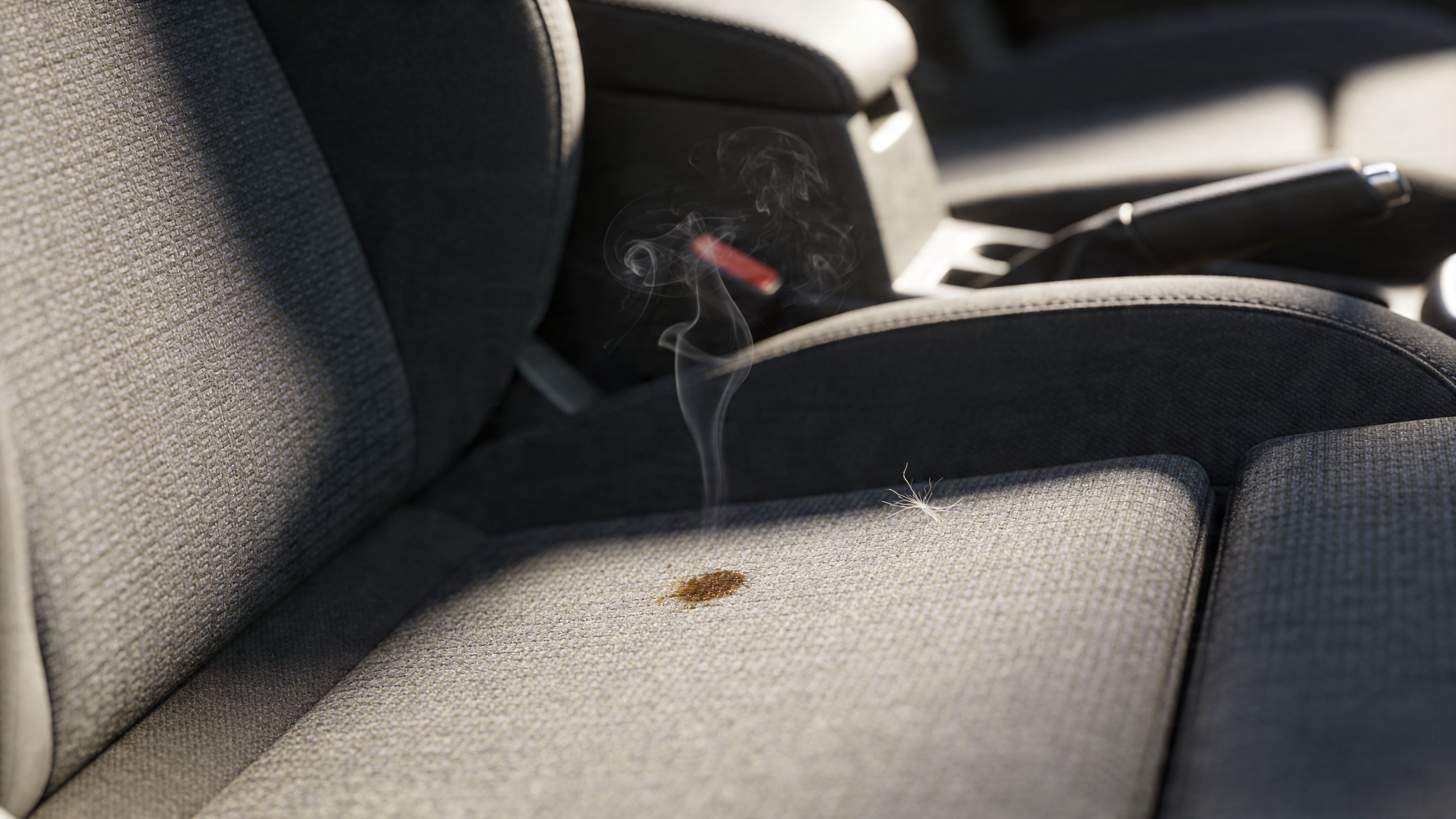 A car seat with a small burn mark emitting thin wisps of smoke in a parked vehicle.