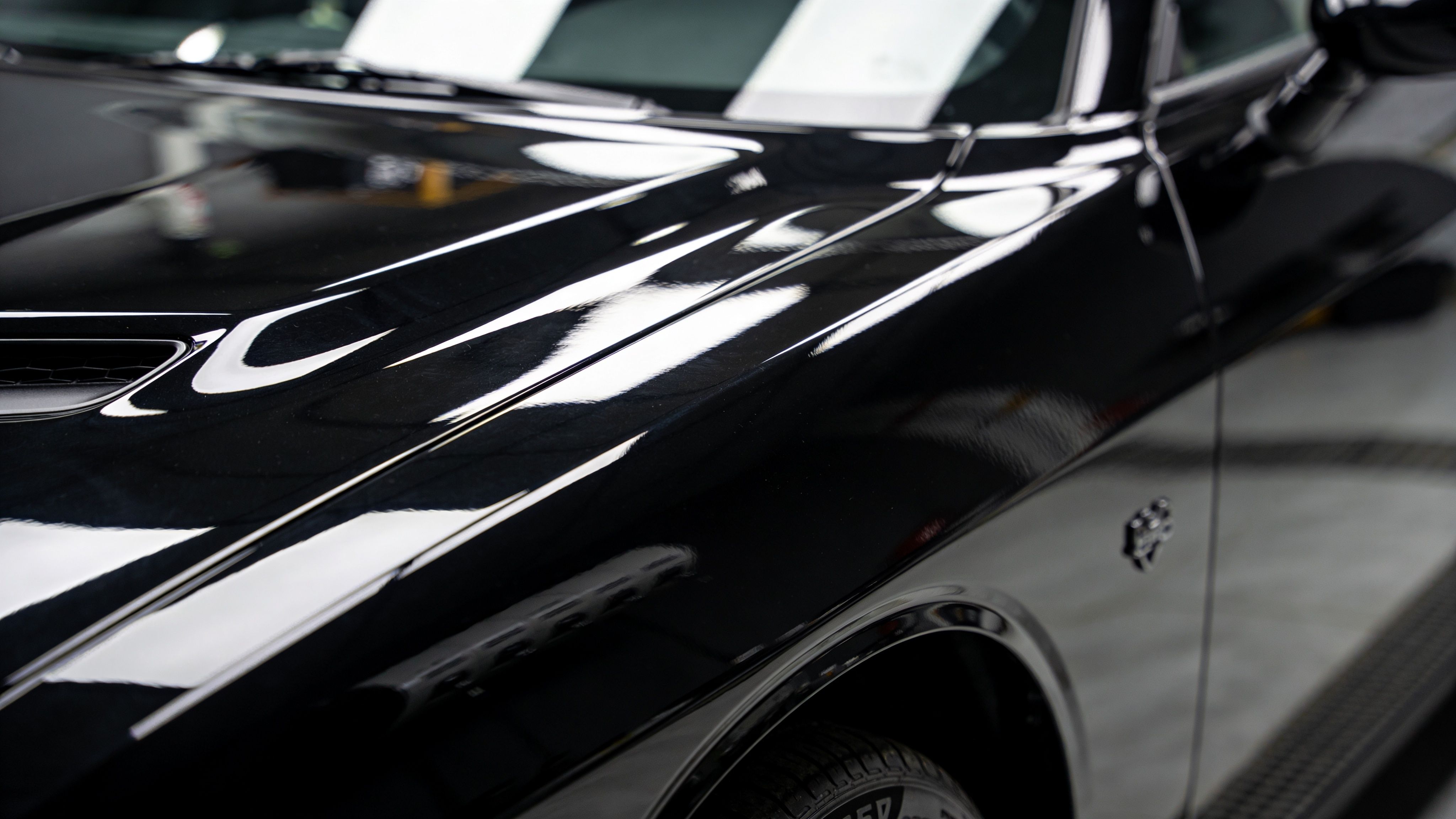 A close-up view of a shiny, polished black car hood and fender in a professional garage.