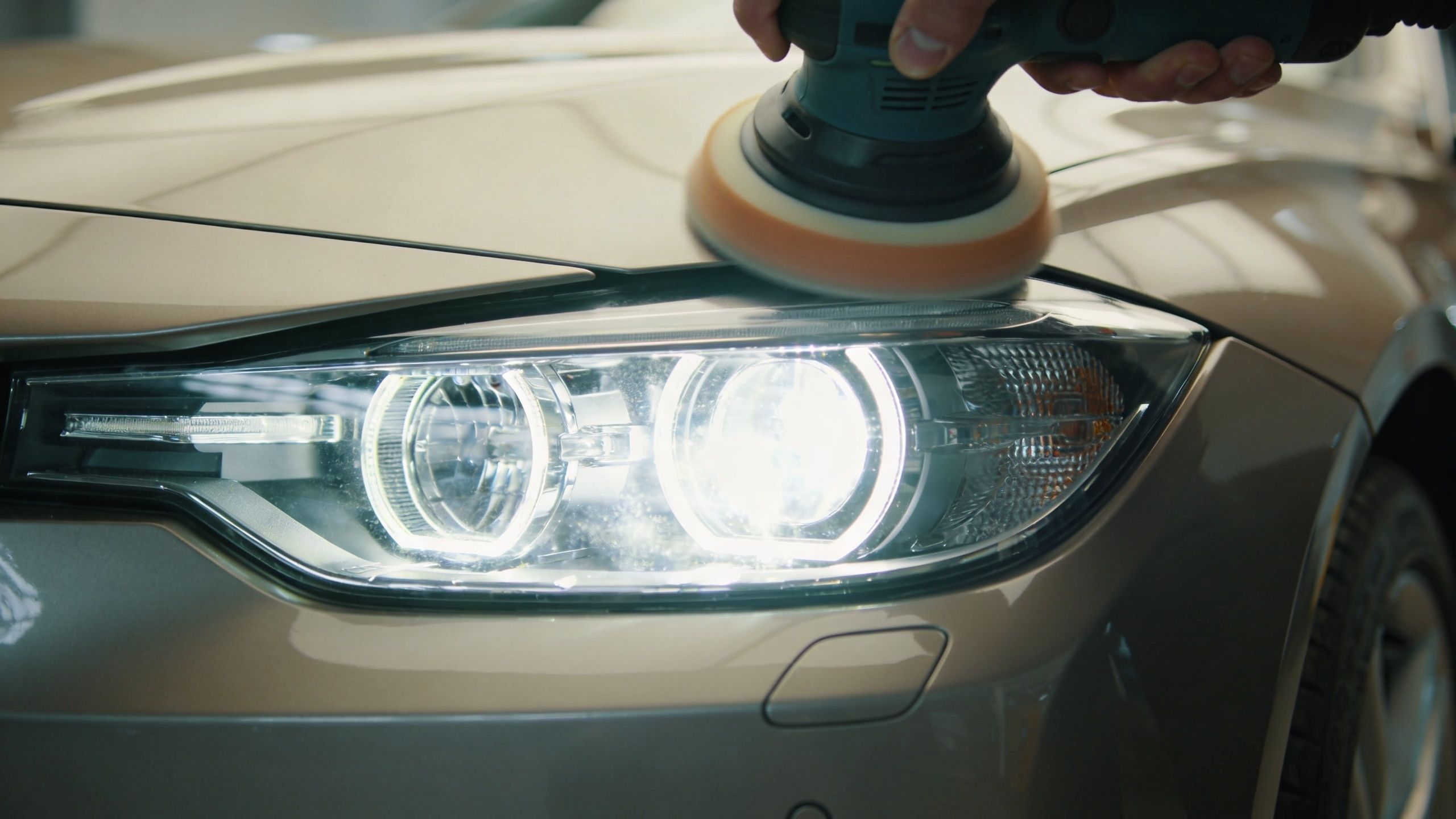 A professional technician using a power buffer to polish and restore the headlight of a car.