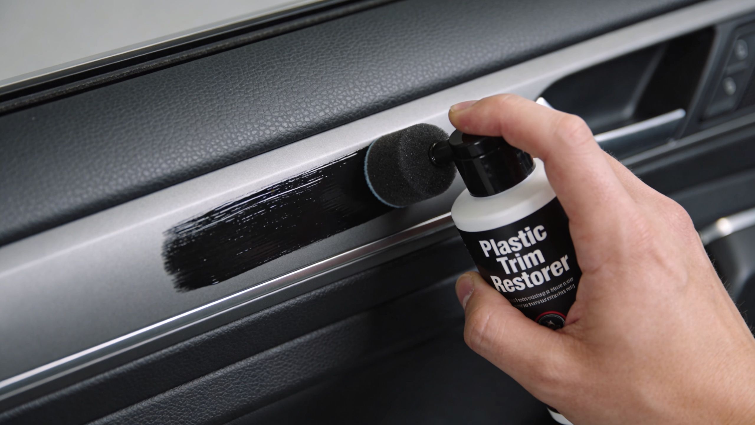 A hand using a small foam applicator to apply black plastic trim restorer to a car interior panel.