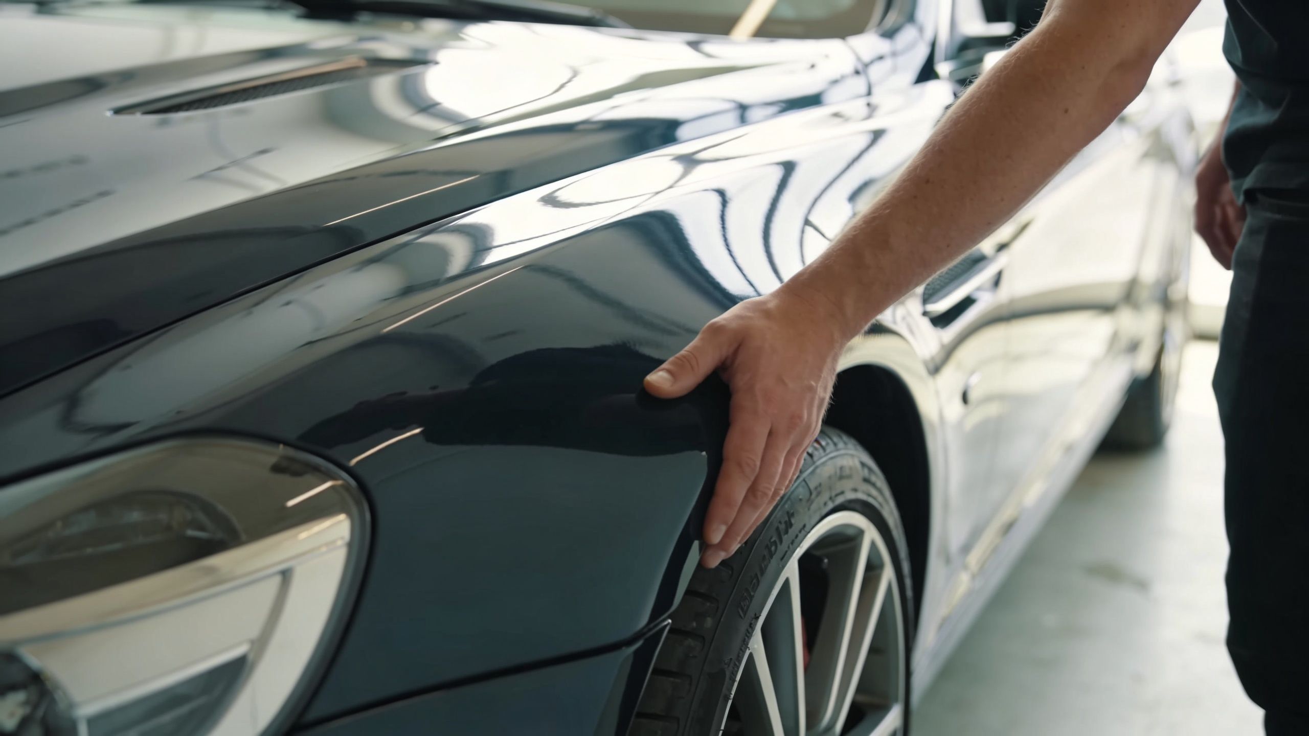 A professional car detailer gently touching the polished surface of a luxury car to inspect the paint quality.
