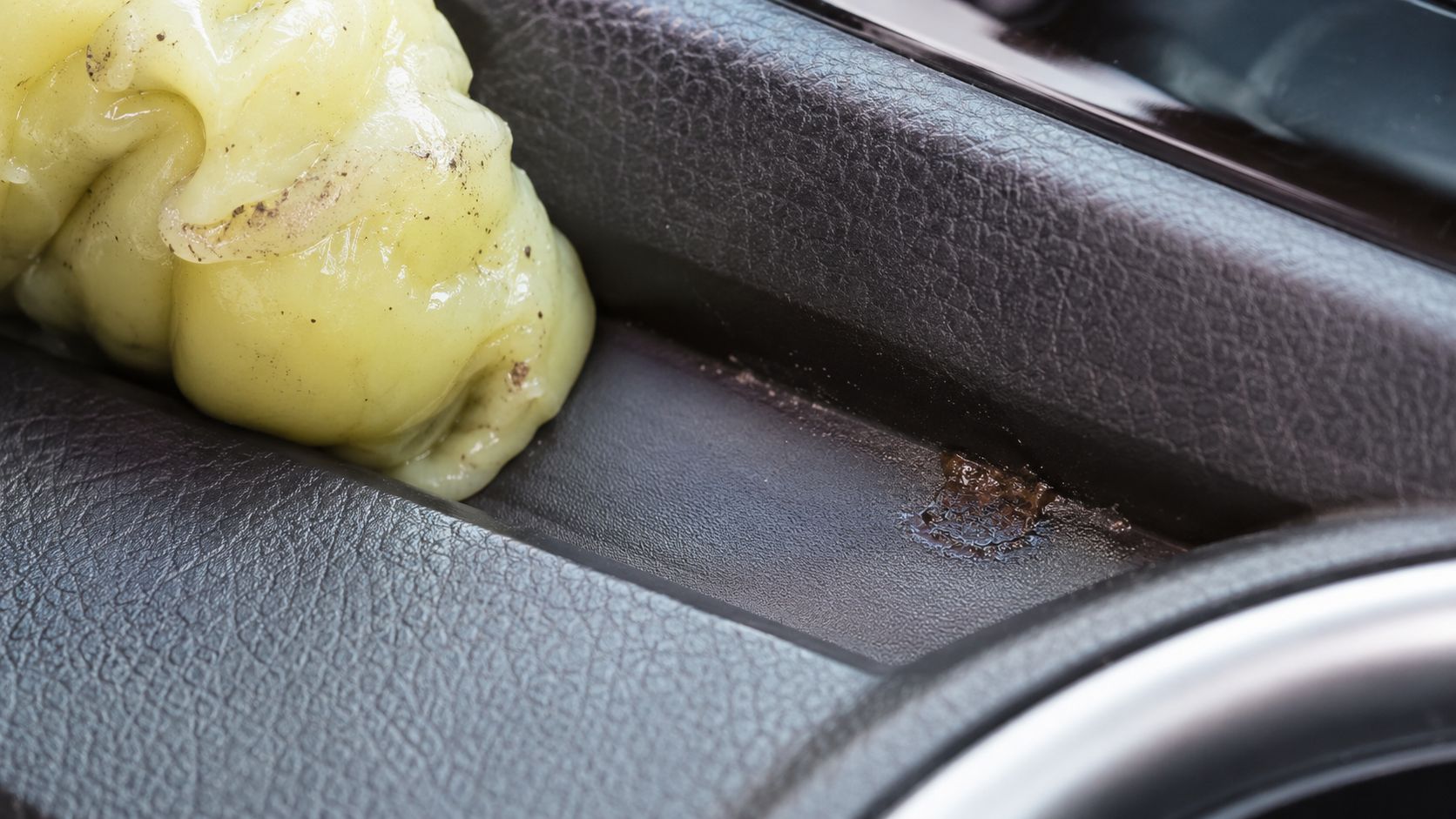 Cleaning putty being used to remove dirt and grime from the dark textured surface of a car interior.