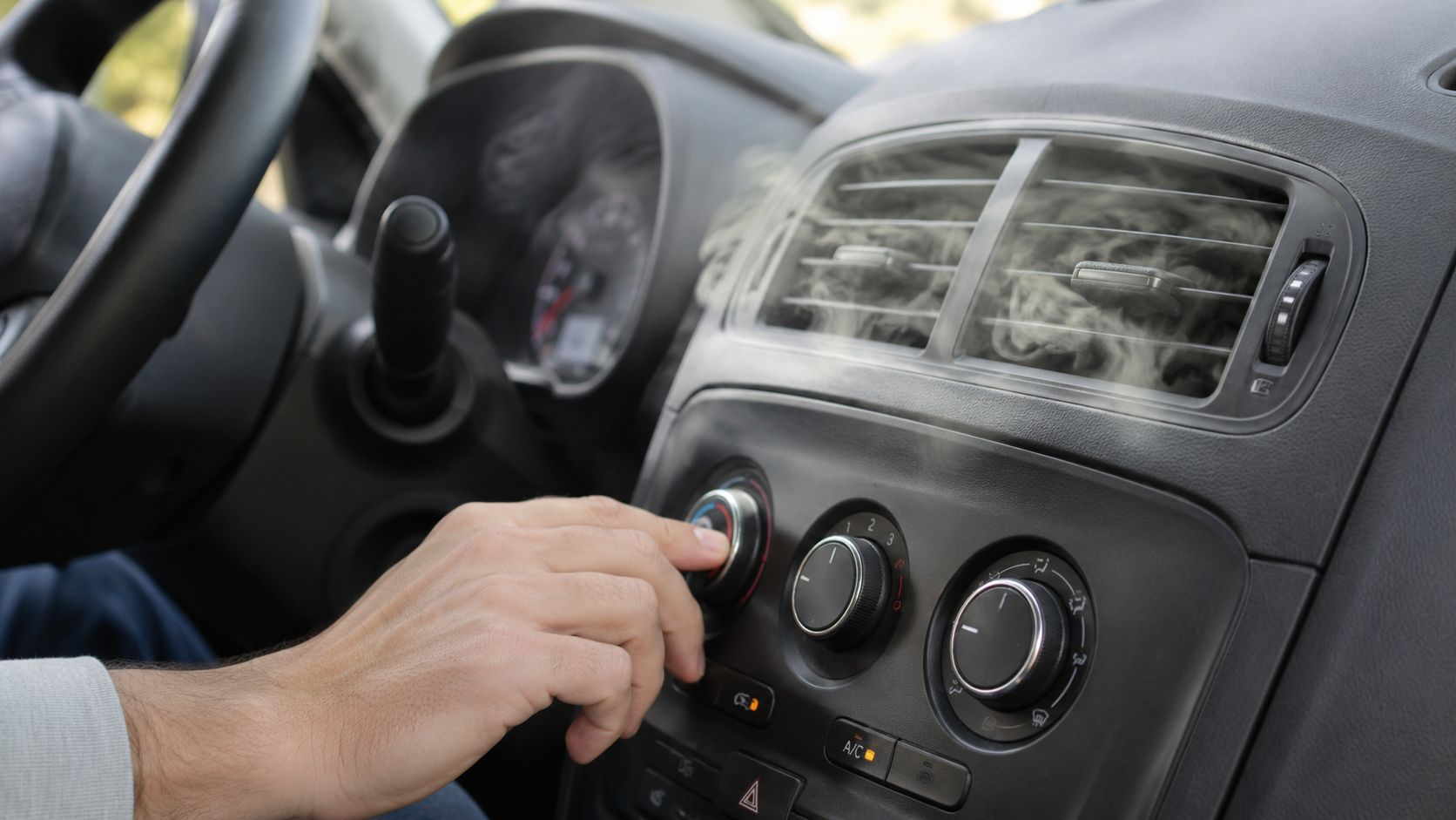 A person adjusting the car air conditioning controls while vapor or cold air flows from the dashboard vents.