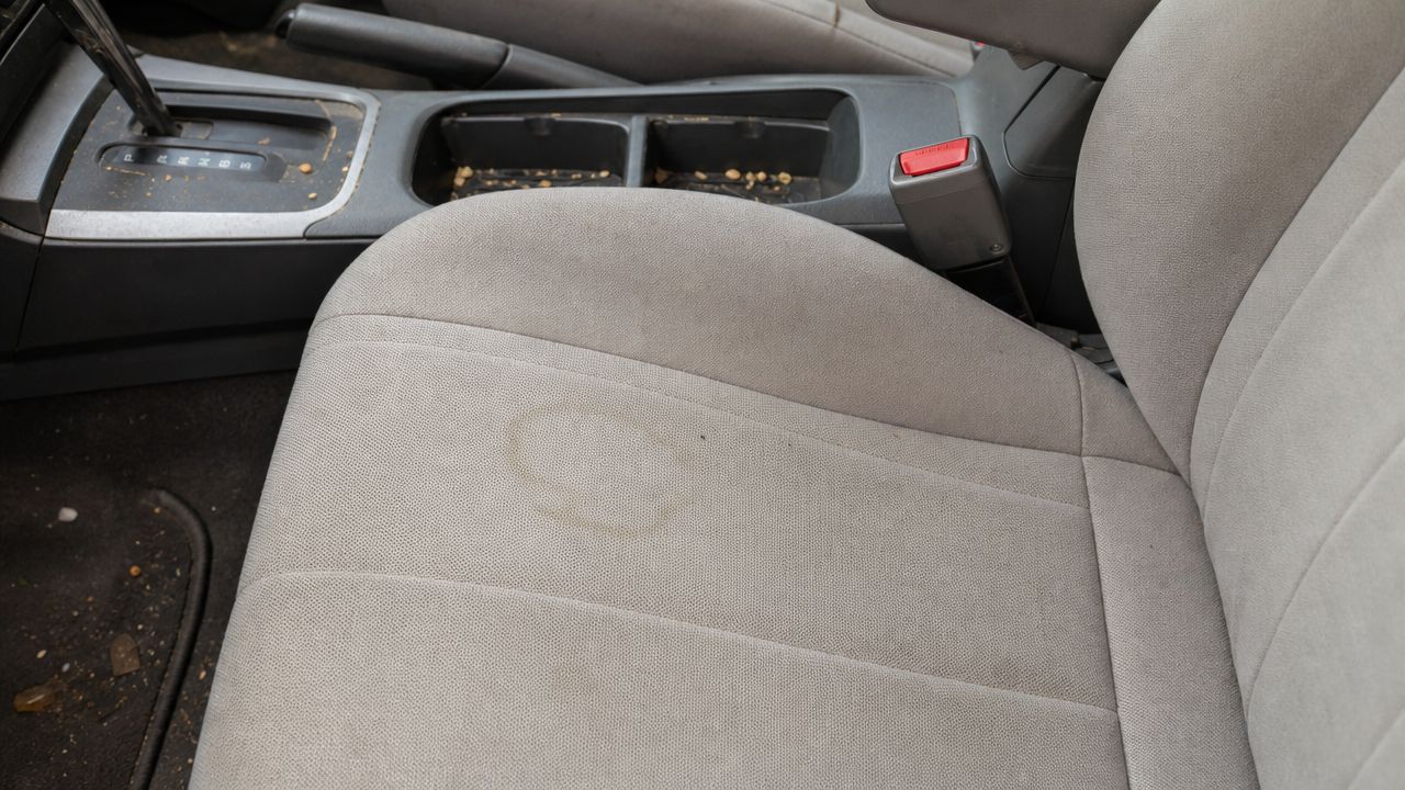 A stained grey car seat with crumbs on the console, illustrating the need for auto detailing.