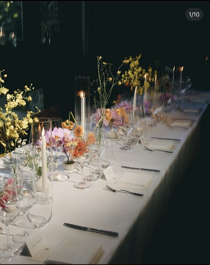 Elegant dining table set with white tablecloth, floral centerpieces, candles, wine glasses, and neatly arranged cutlery.