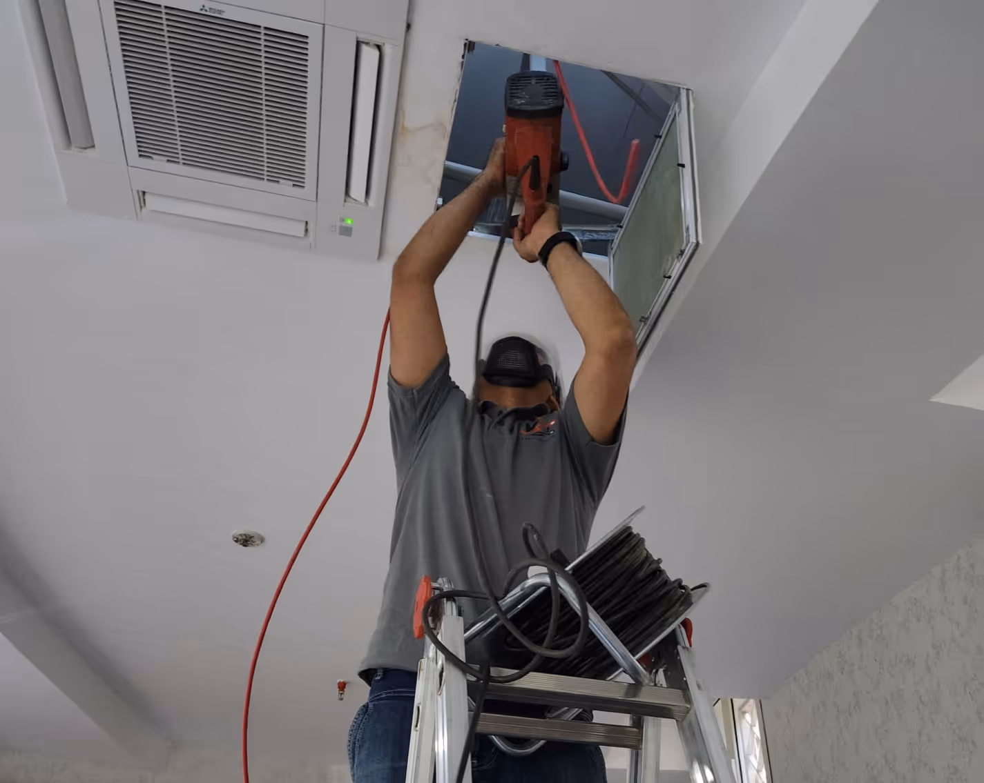 A worker drilling the ceiling to install fire protection equipment
