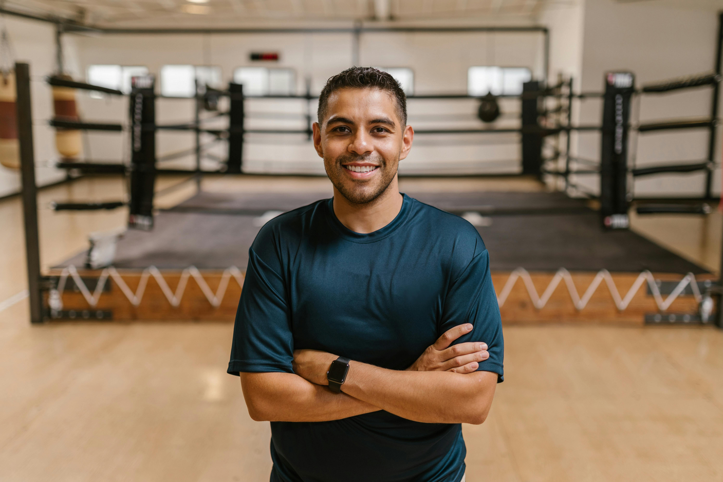 Trainer standing with arms crossed in front of a boxing ring. 
