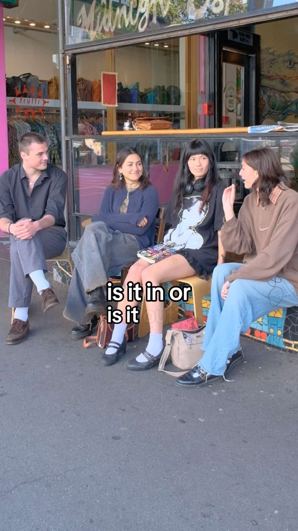 A still from a video showing three young people being interviewed by a fourth on a bench on a pavement.