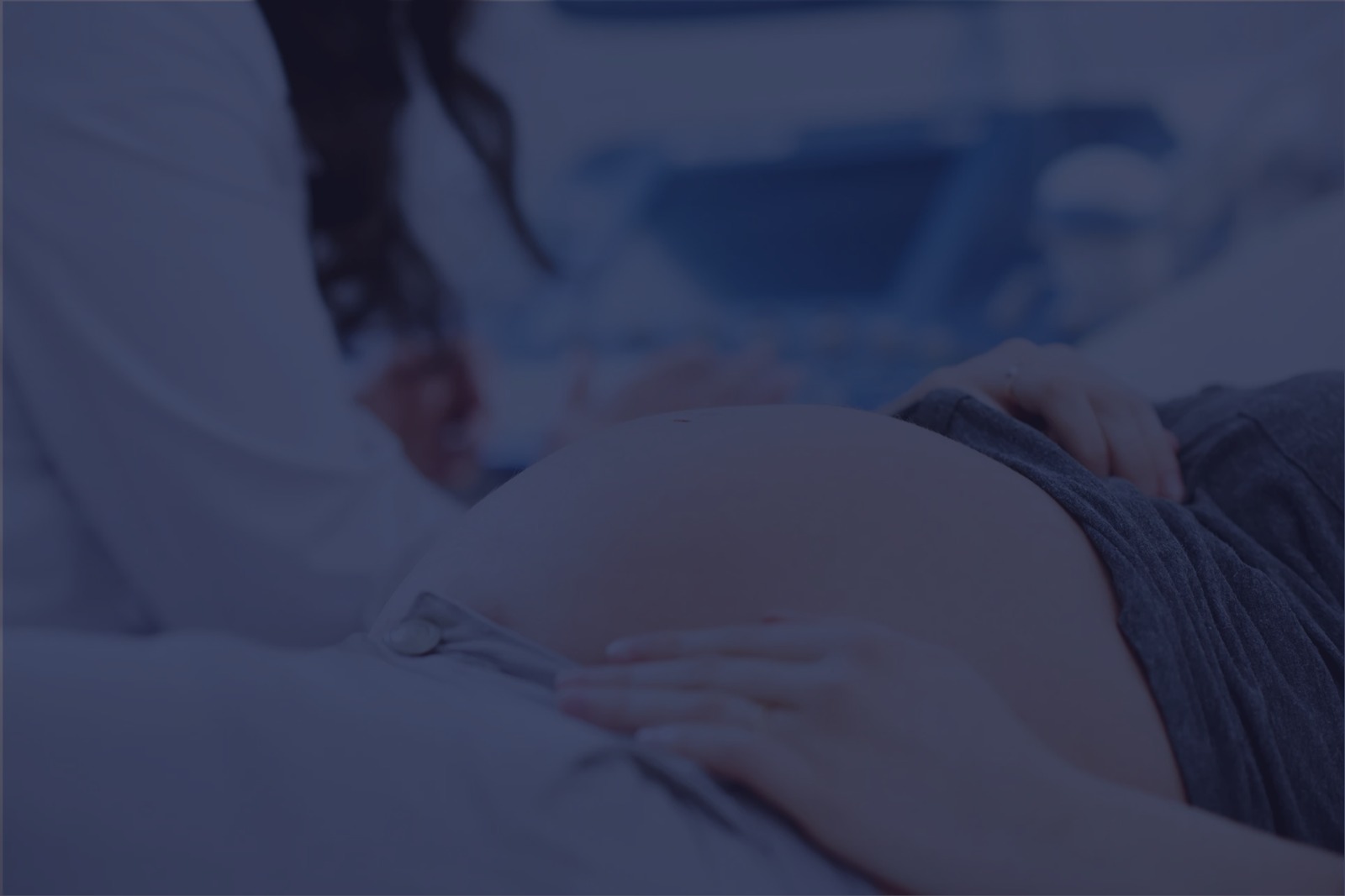Pregnant woman lying down with hands on her belly, healthcare professional sitting nearby.