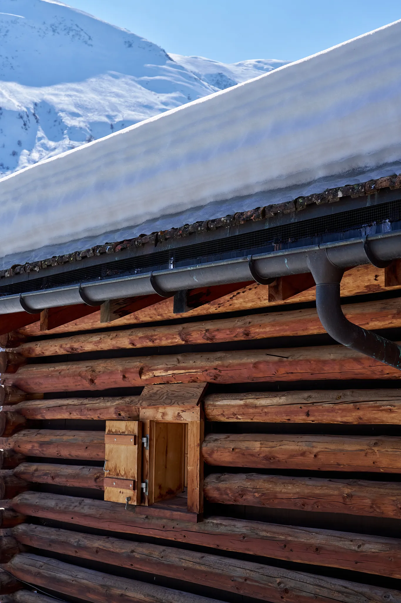Verschneite Berghütte mit Holzwänden und Dachrinnen im Winter