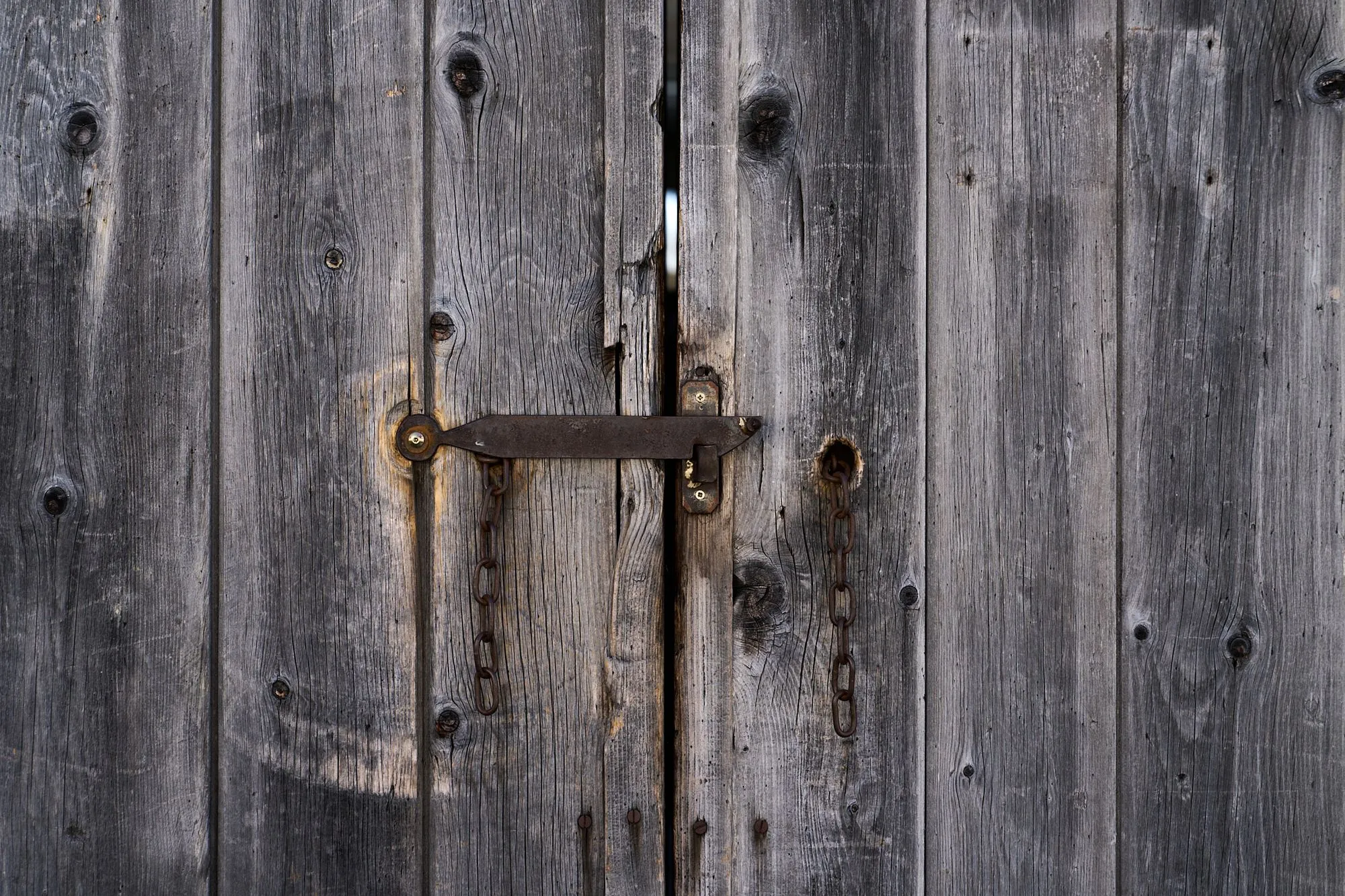 Alte graue Holztür mit Metallriegel und Ketten, verwittert und robust