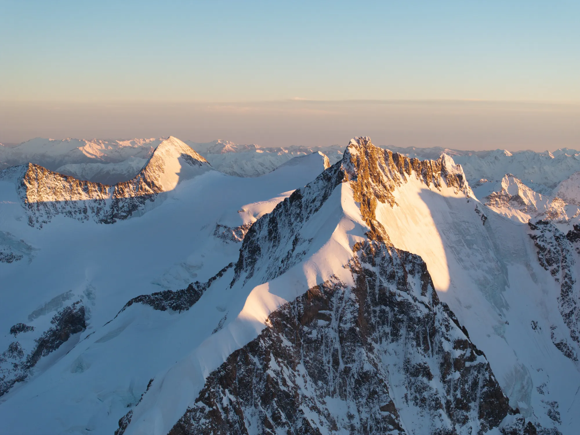 Schneebedeckte Berggipfel im warmen Licht des Sonnenuntergangs mit klarem Himmel.