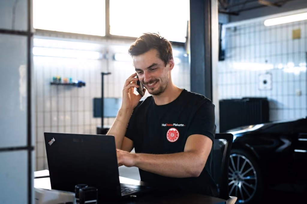 Ein lächelnder Mann, der mit einem Kunden spricht, während er seinen Termin für eine Hauptuntersuchung auf einem Laptop plant